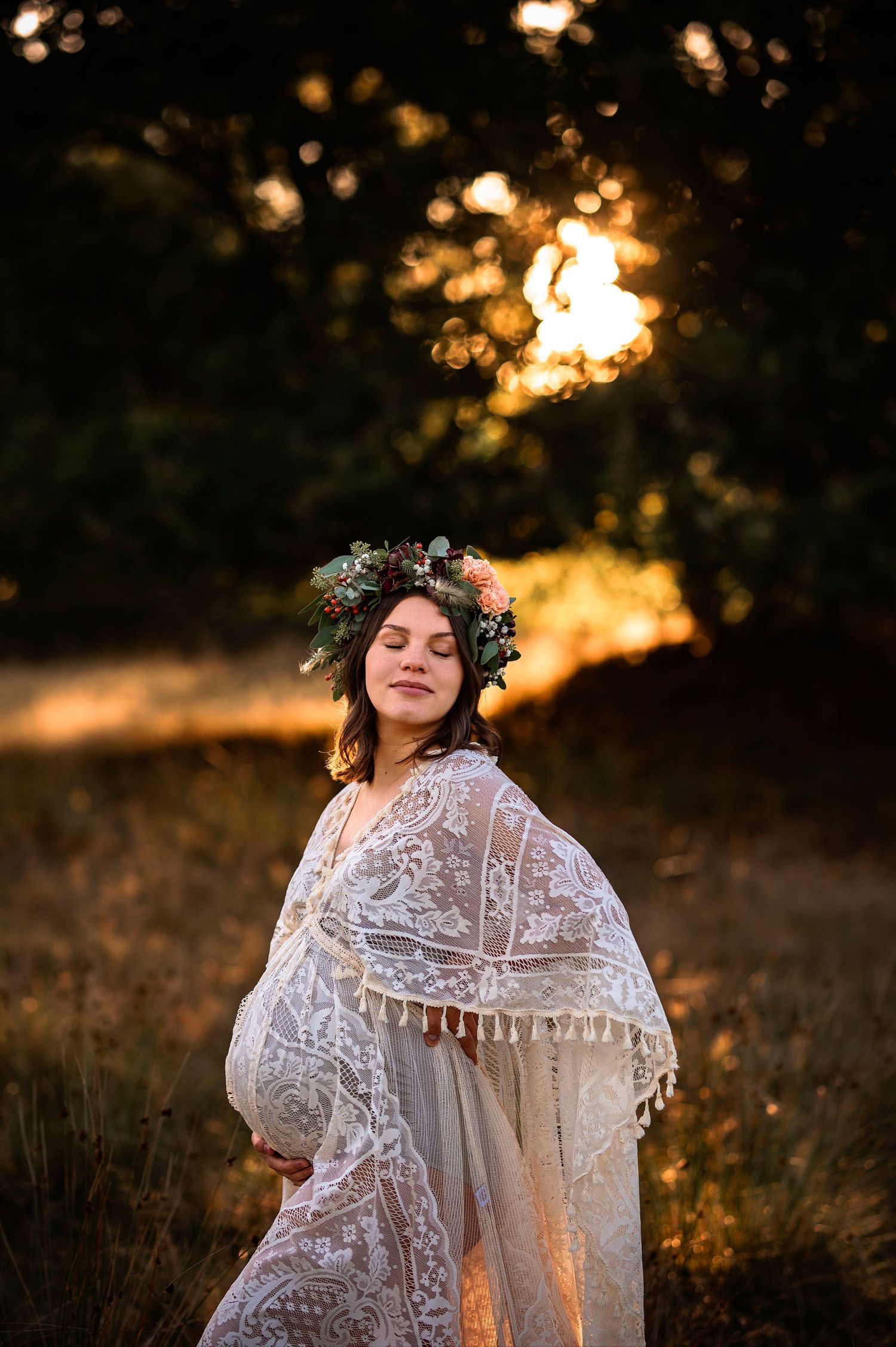 Gravidfotografering i Skåne med motljusporträtt av blivande mamma i blomsterkrans i gyllene solnedgång.