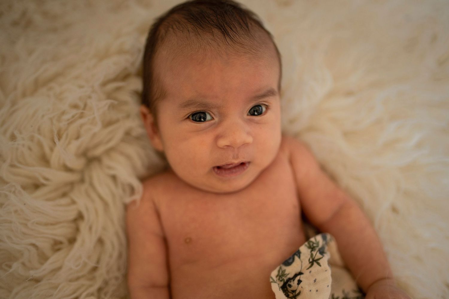 Happy baby with bright eyes laying on soft furry blanket.
