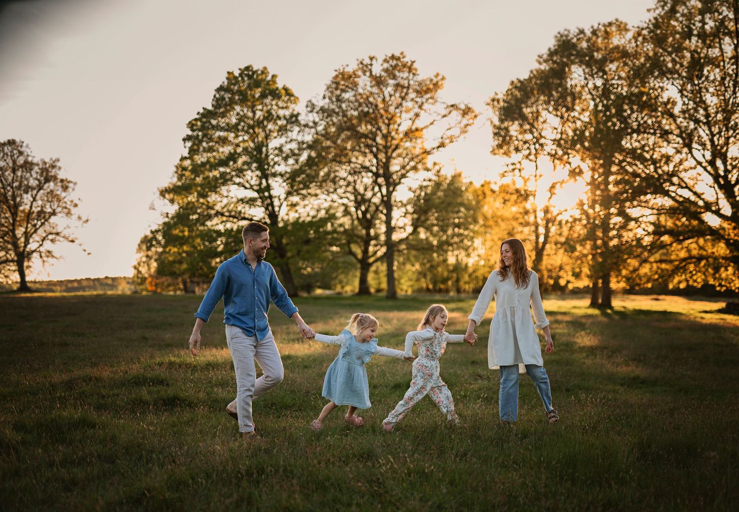Familjefotografering i Skåne med familj som går hand i hand i solbelyst höstäng i gyllene kvällsljus.