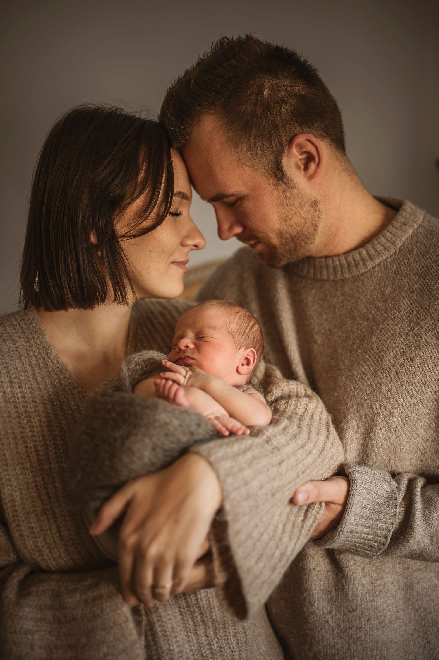 Nyblivna föräldrar håller sin nyfödda bebis under en nyföddfotografering i Hässleholm i en kärleksfull stund.