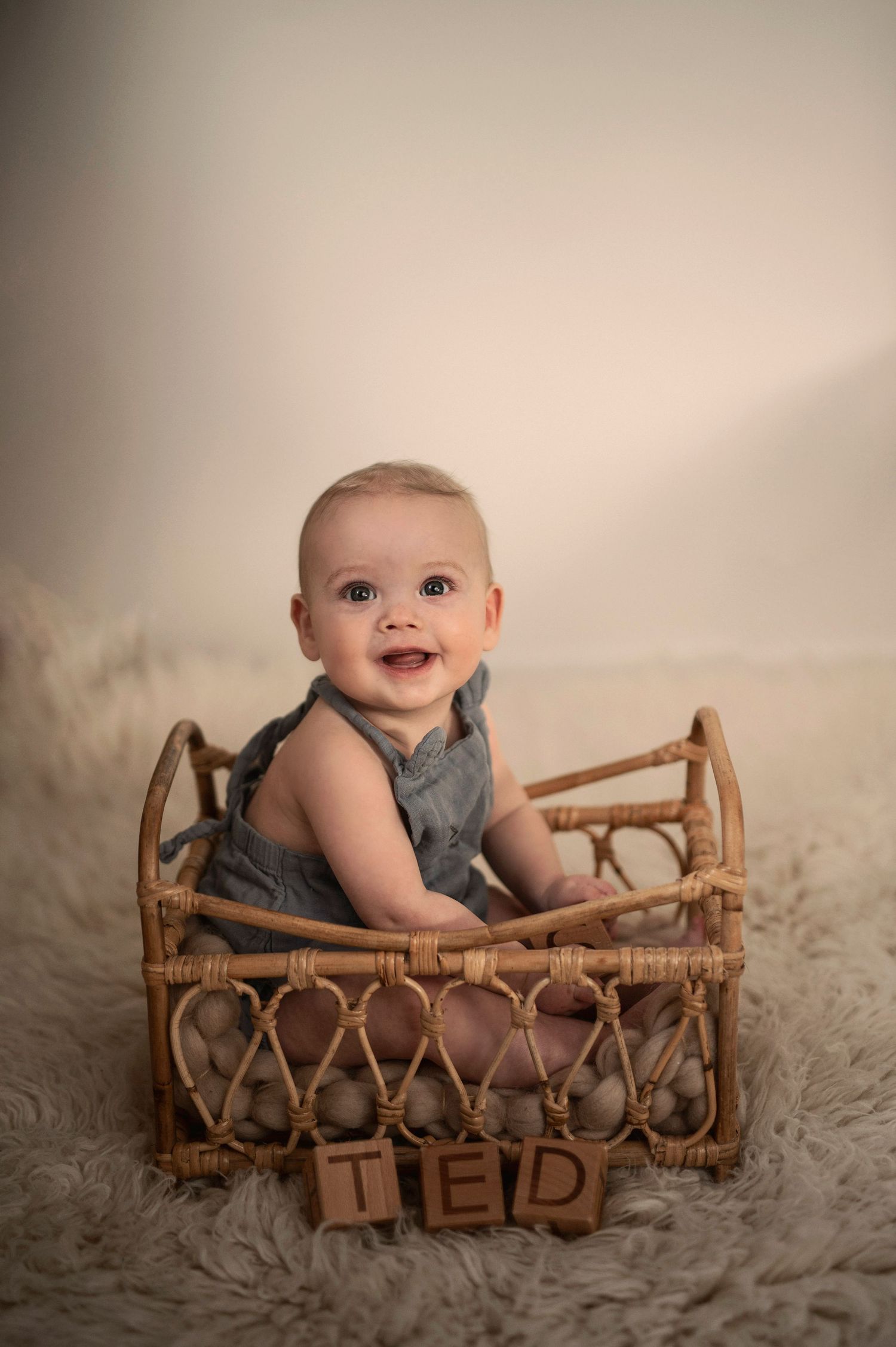 Ettårsfotografering i Hässleholm med leende bebis i korg och grå denimromper i studio.