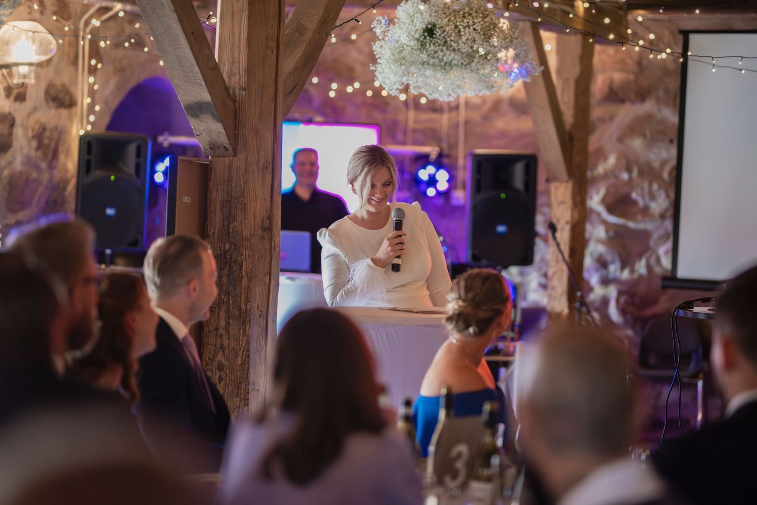 Bröllopsfotografering i Skåne med brud som håller tal under rustik bröllopsfest med ljusslingor.