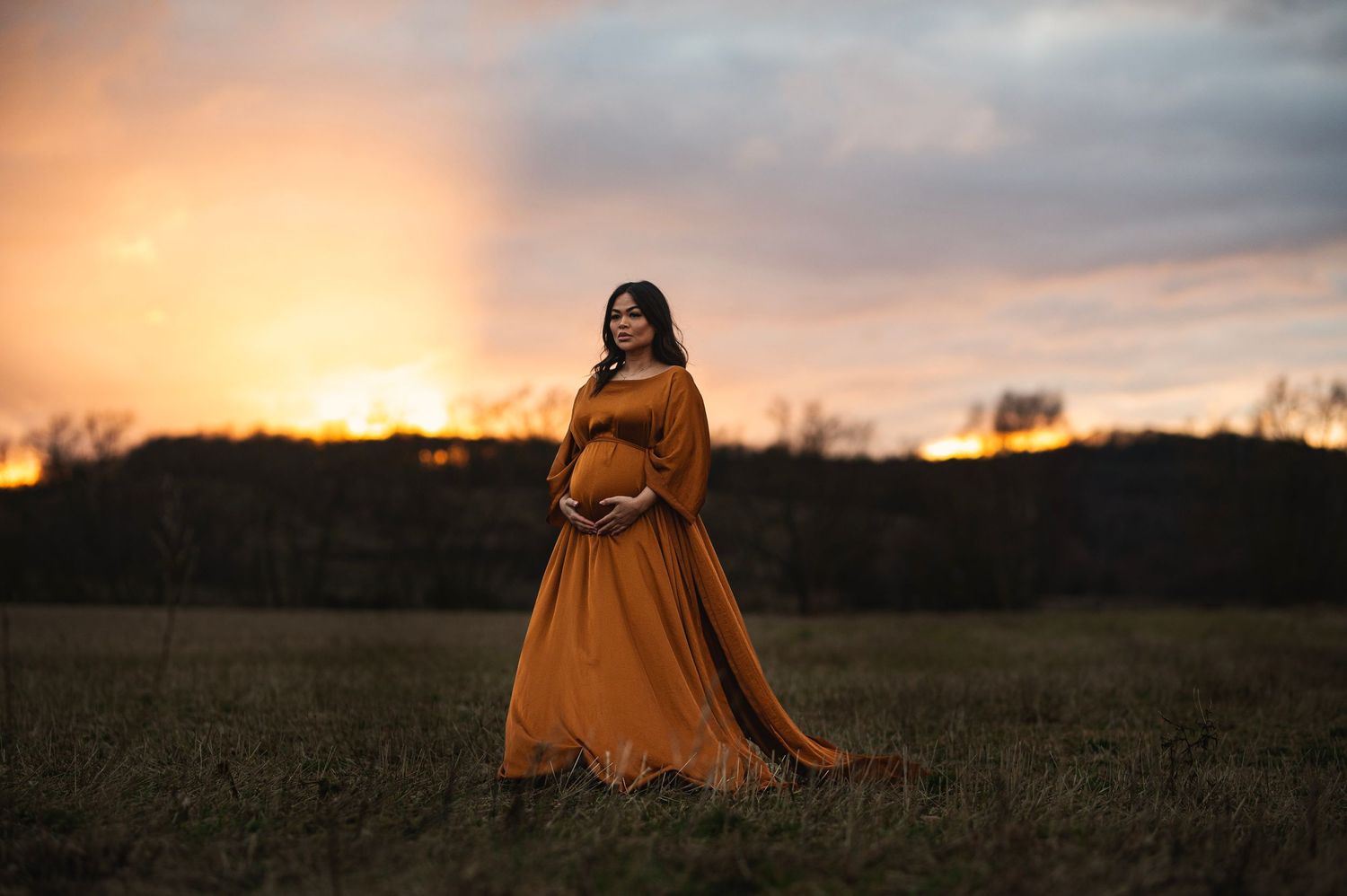 A maternity portrait featuring a flowing orange dress against a dramatic sunset sky.