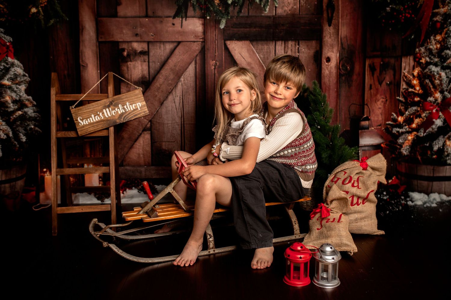 Two children sit together on a vintage sled in a festive Christmas studio portrait with holiday decorations.