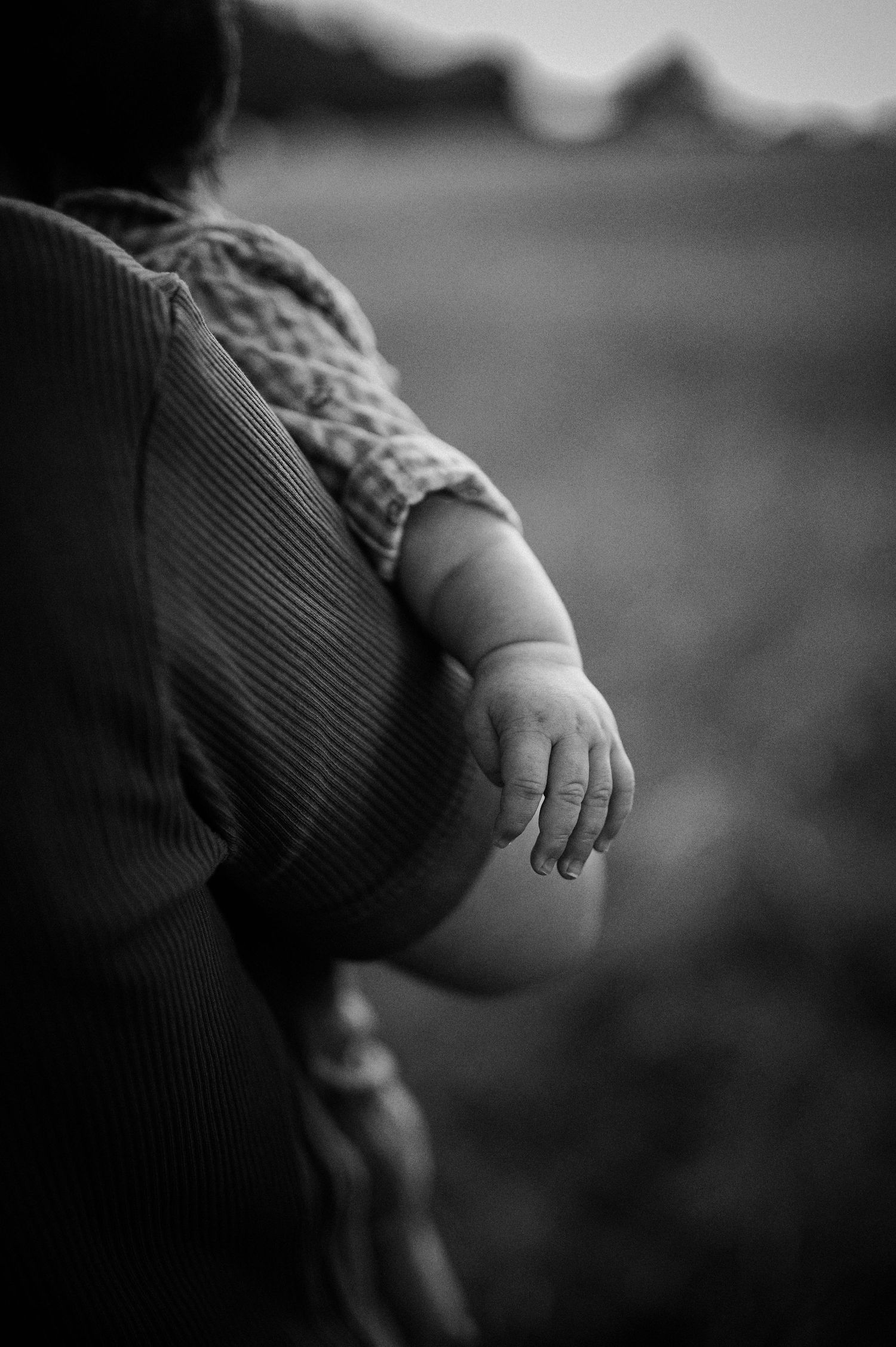 Nyföddfotografering i Skåne med bebis hand som håller vuxens arm i svartvitt närbild.
