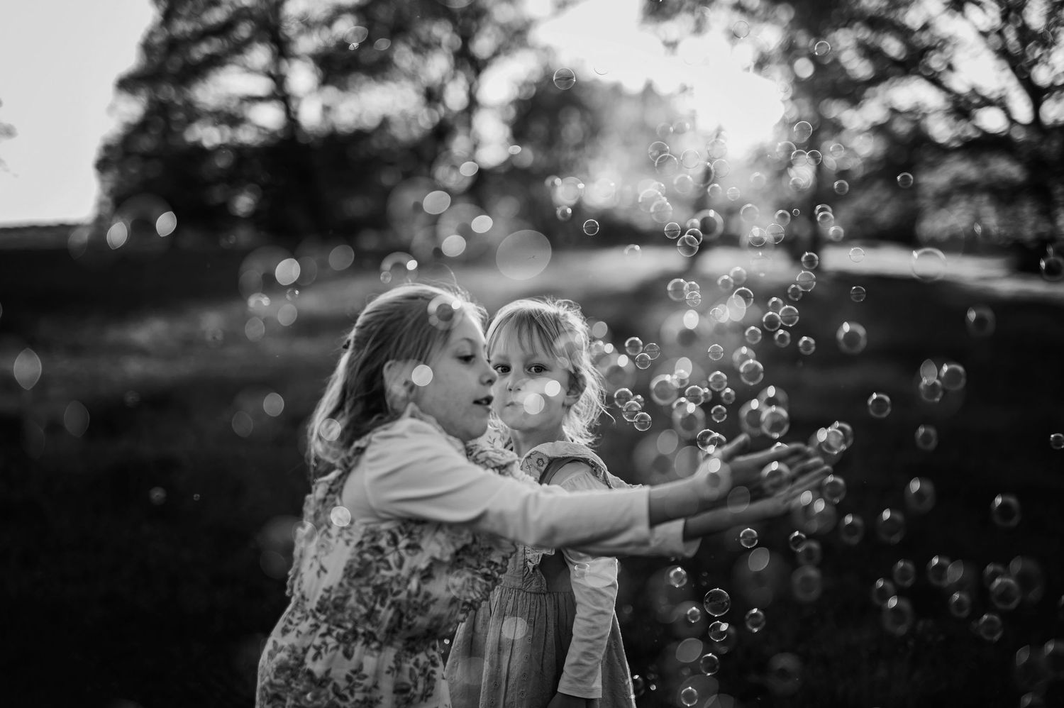 Familjefotografering i Skåne med syskon som blåser såpbubblor i en hage i svartvitt ljus.