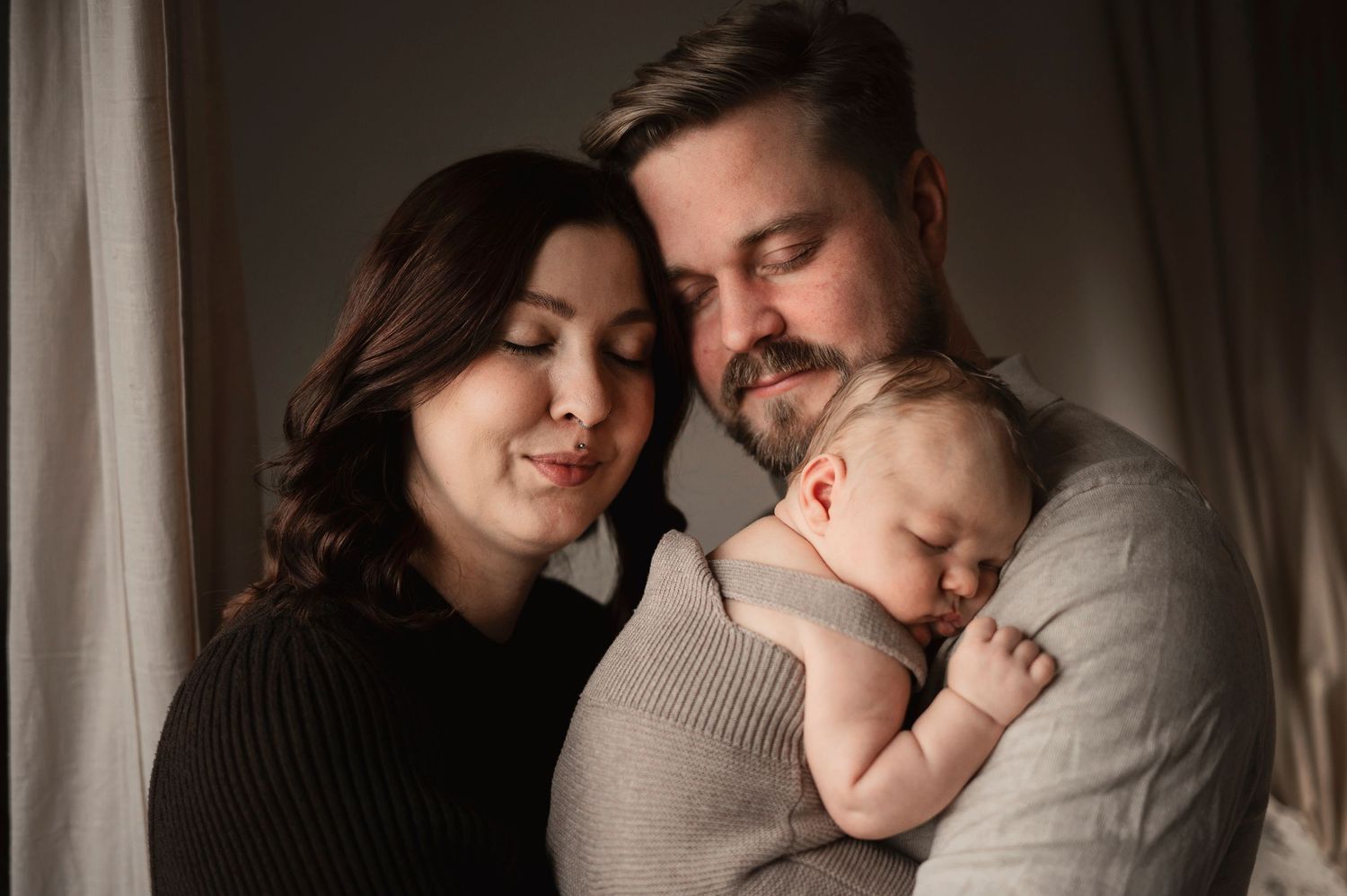 Nyblivna föräldrar håller sin sovande nyfödda bebis under en nyföddfotografering i Hässleholm i dagsljus studio med mjukt ljus.
