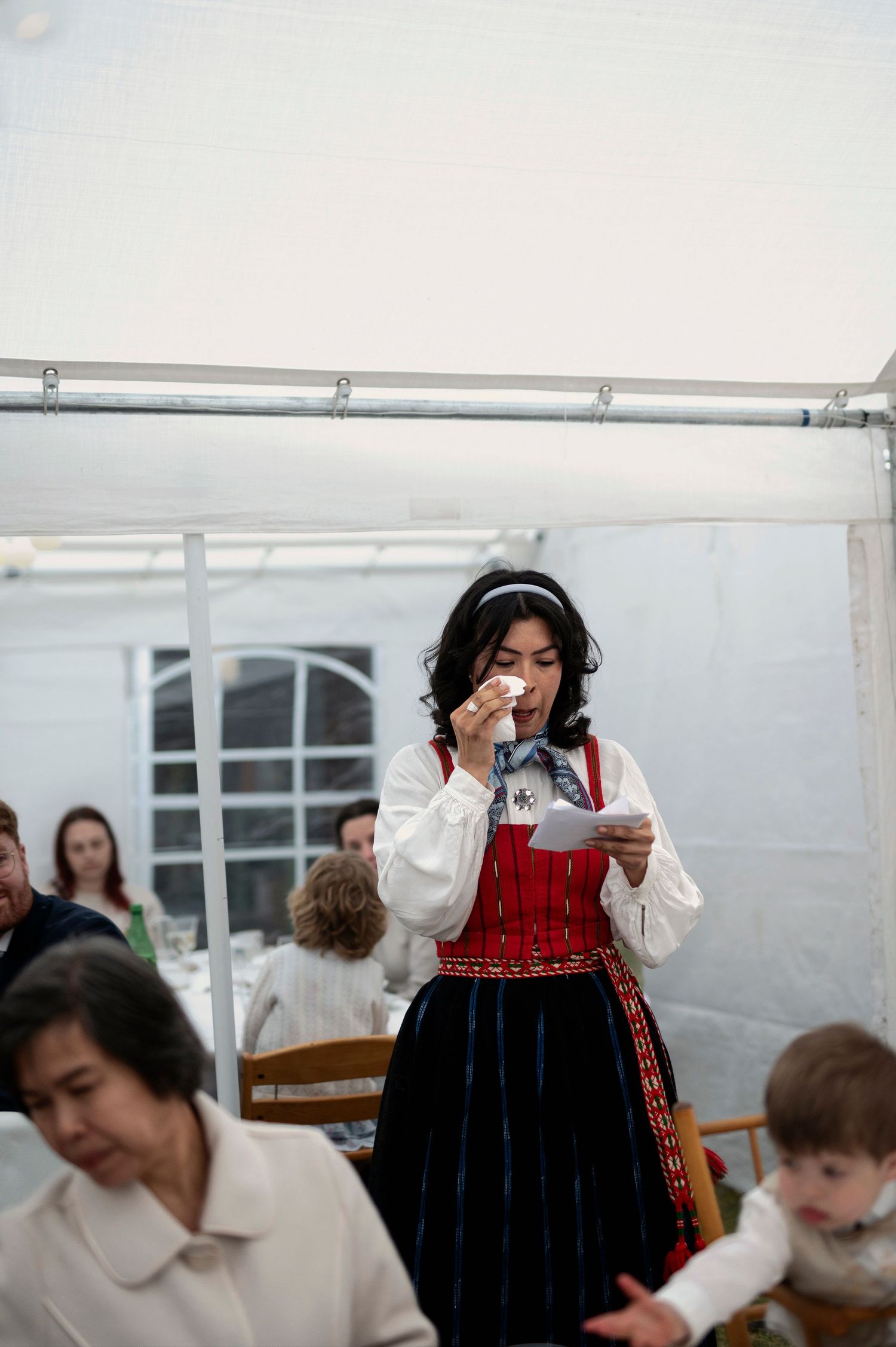 Bröllopsfotografering i Skåne med kvinna i folkdräkt som håller tal och torkar tårar under bröllopsfest.