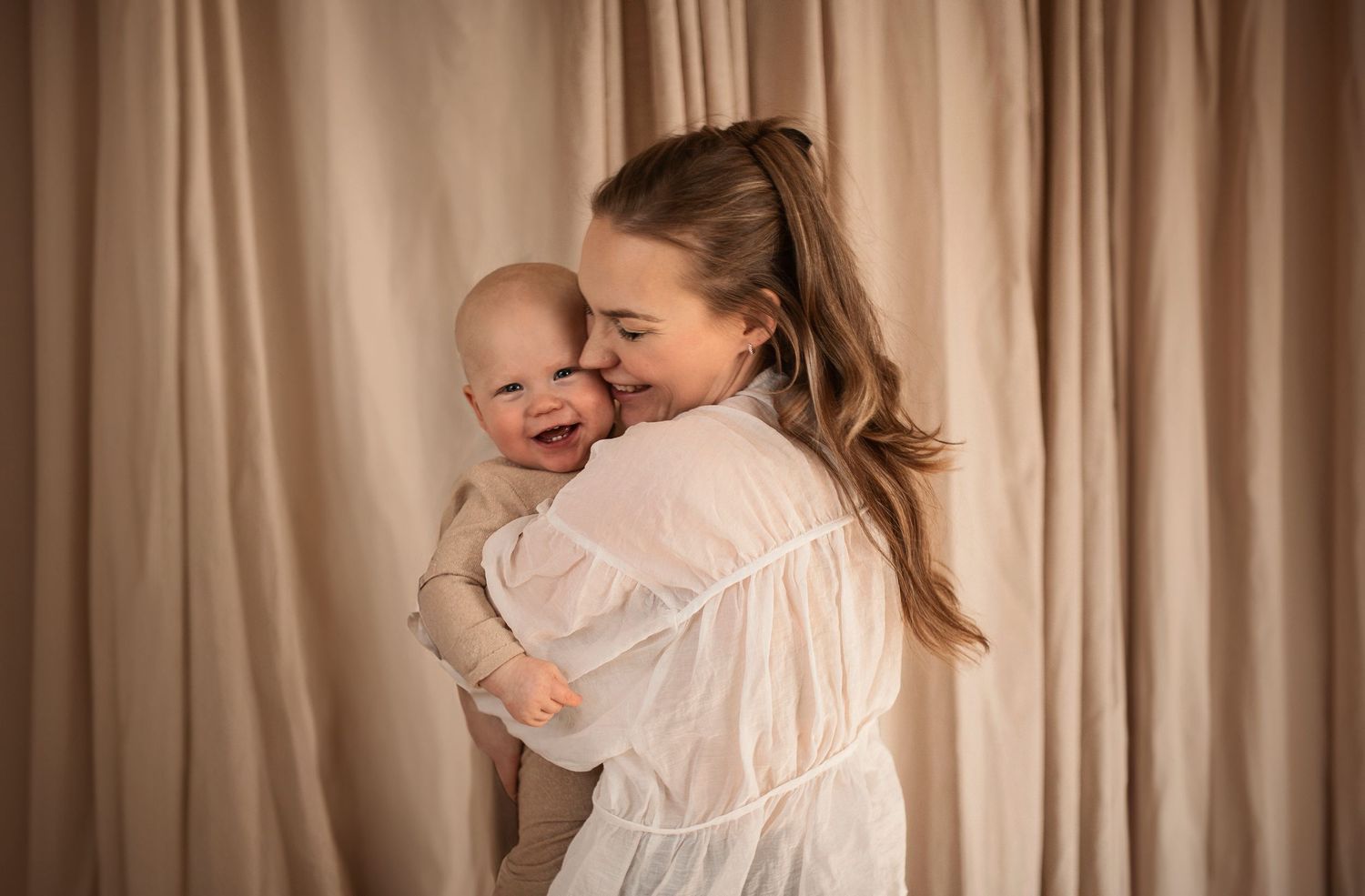 Familjefotografering i Hässleholm med mamma och skrattande bebis i mjukt studioljus.
