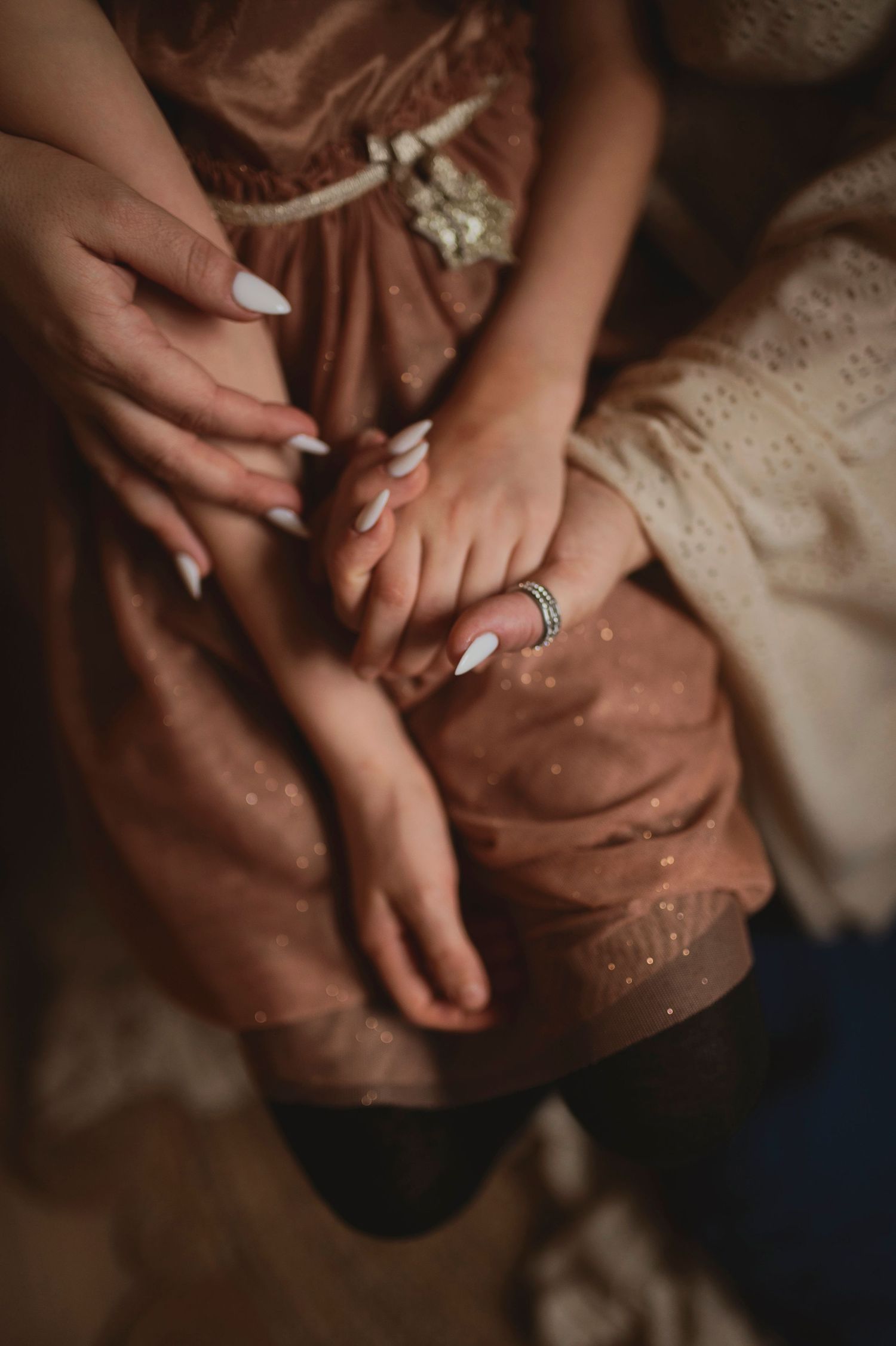 Close-up of hands with white nail polish resting on a pink dress with delicate details.