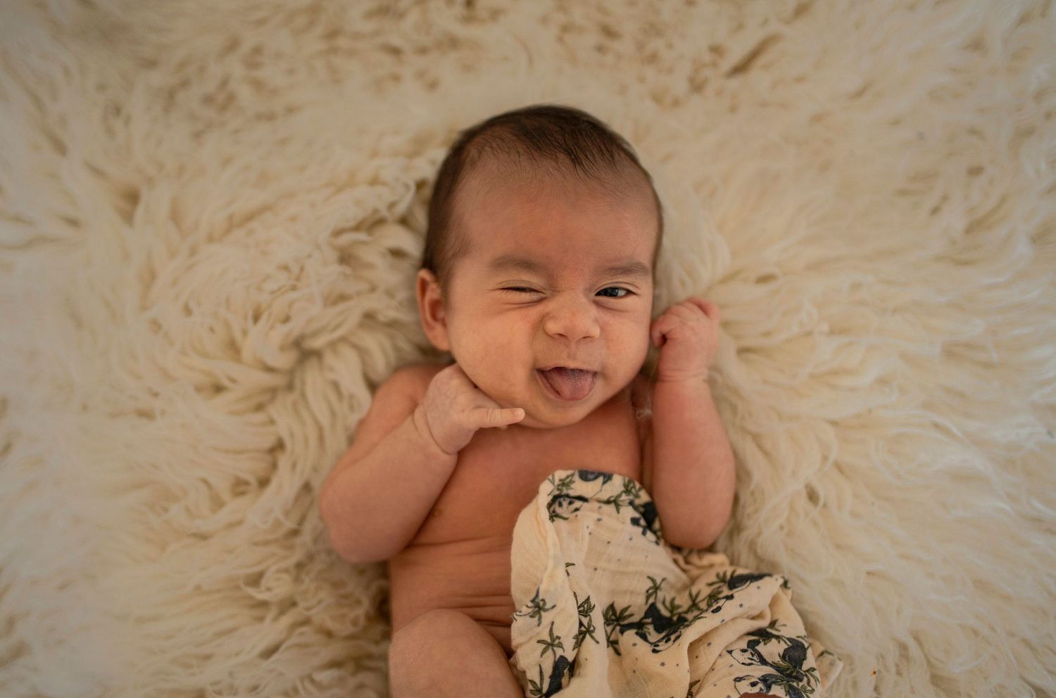 Smiling baby laying on cream colored fur rug during professional photo session.