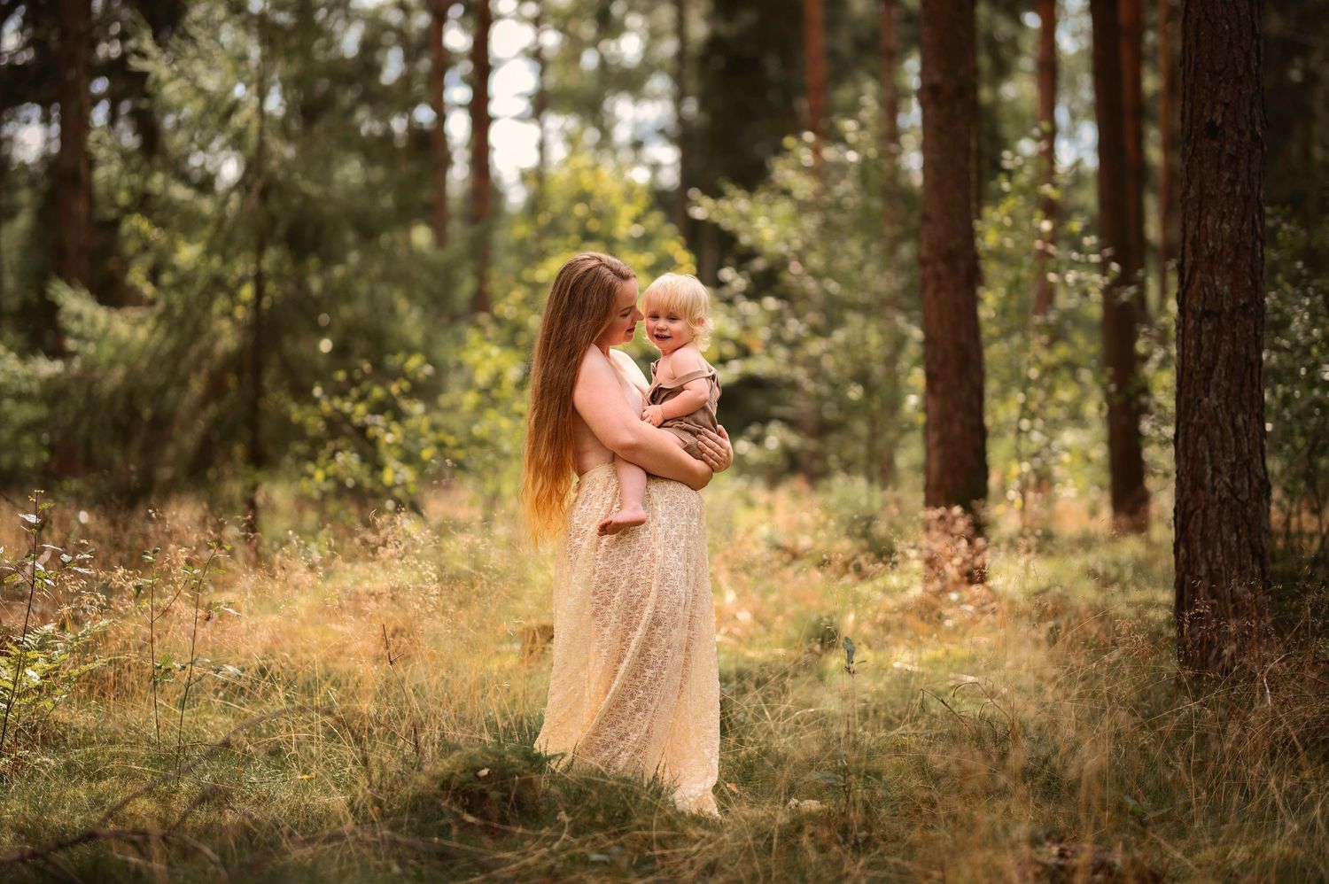 Familjefotografering i Skåne med mamma som håller sitt barn i solbelyst skog i mjukt naturligt ljus.