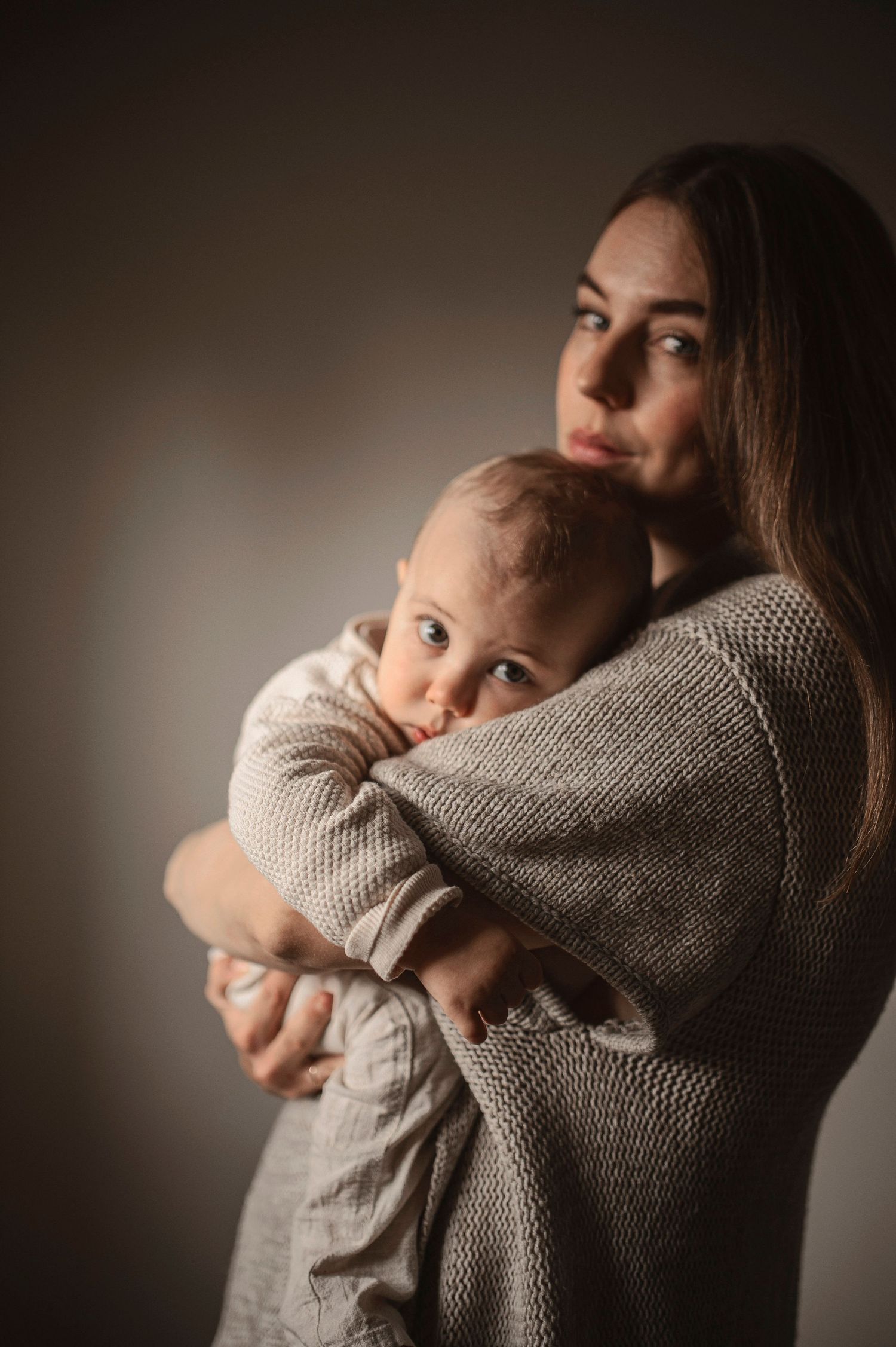 Familjefotografering i Hässleholm med mamma som håller sitt barn i varm studiomiljö.