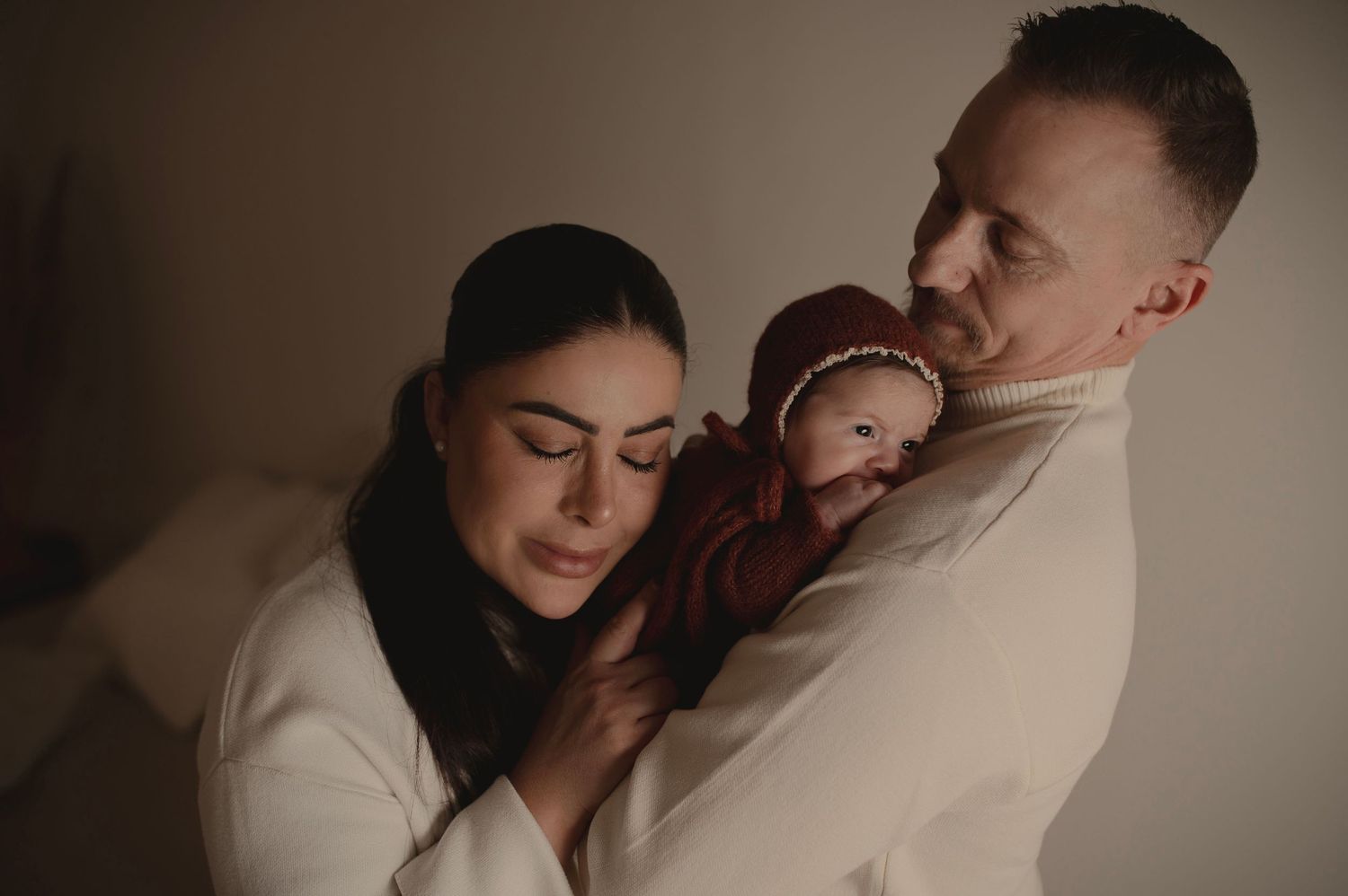 Intimate family portrait in neutral tones with baby in burgundy outfit.