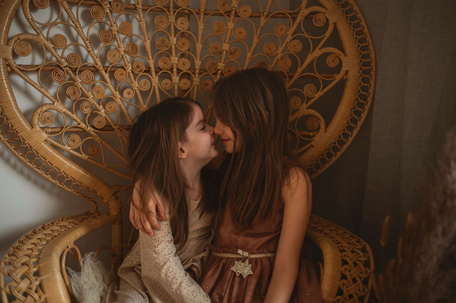 Two people share an intimate moment against a vintage peacock chair backdrop in warm lighting.