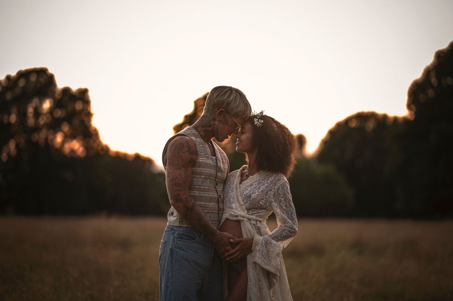 Parfotografering i Skåne med romantiskt par i gyllene solnedgång på äng med träd i bakgrunden.