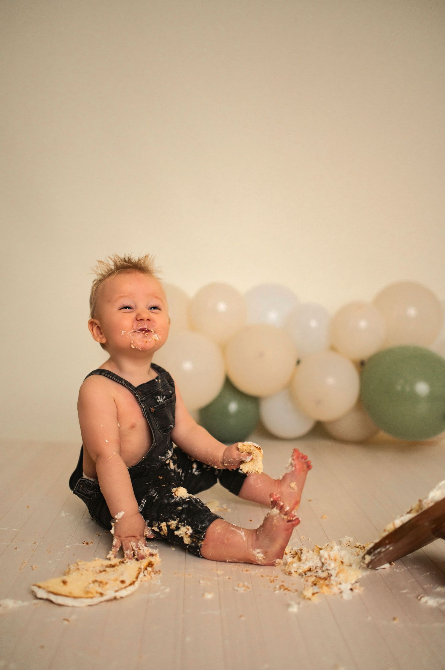 A joyful cake smash finale with frosting-covered overalls and scattered cake pieces.