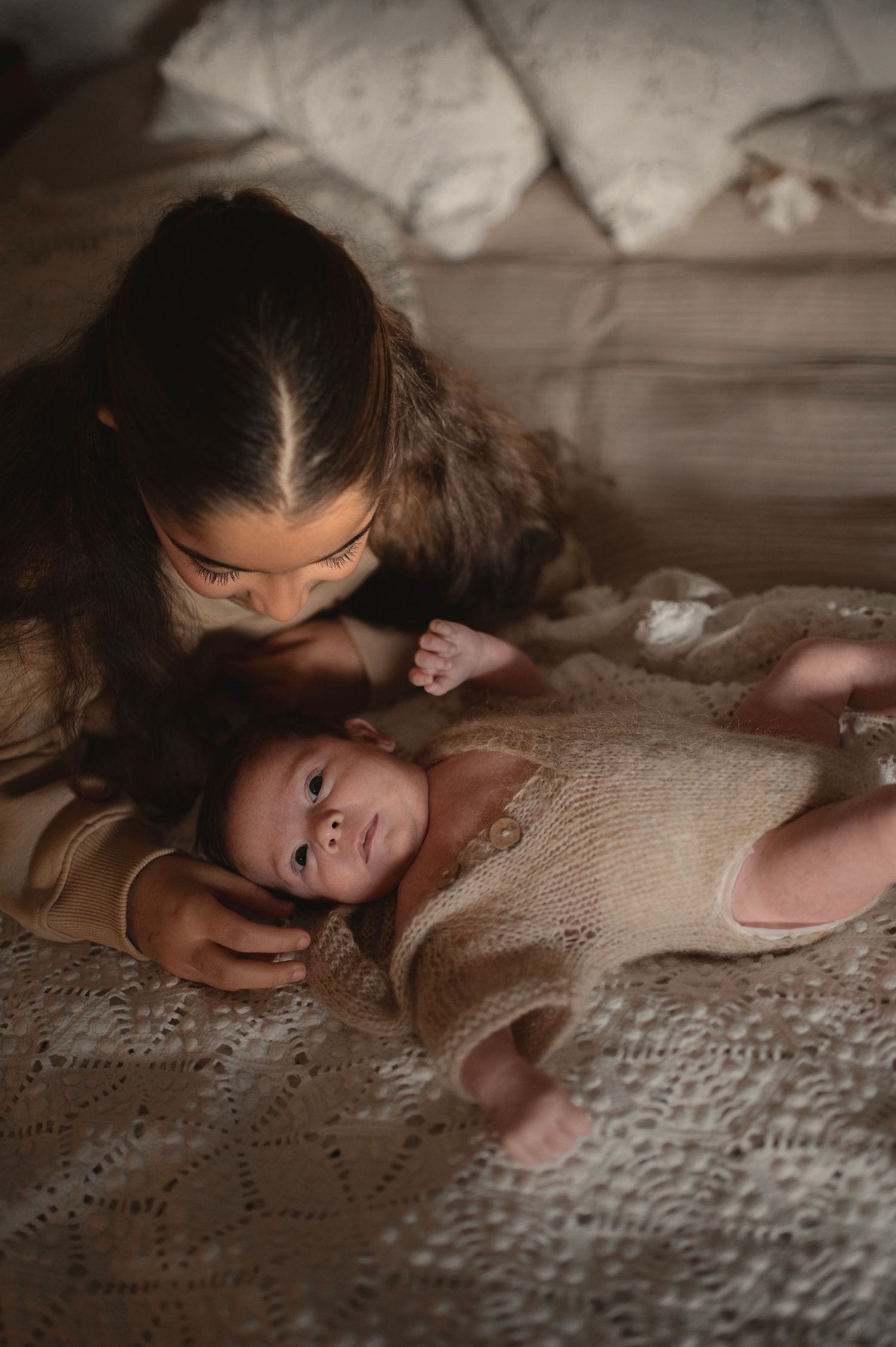 Intimate portrait of nurturing moment on textured bedding with warm lighting.