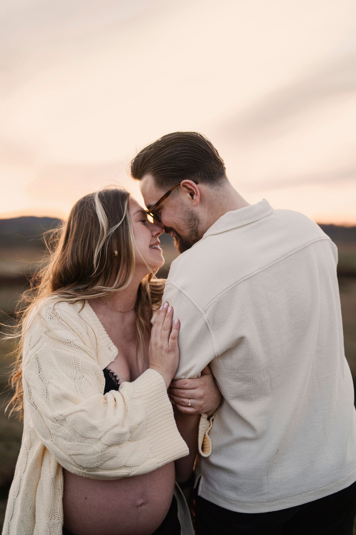 Gravidfotografering i Skåne med blivande föräldrar i blåsig äng i gyllene kvällsljus.