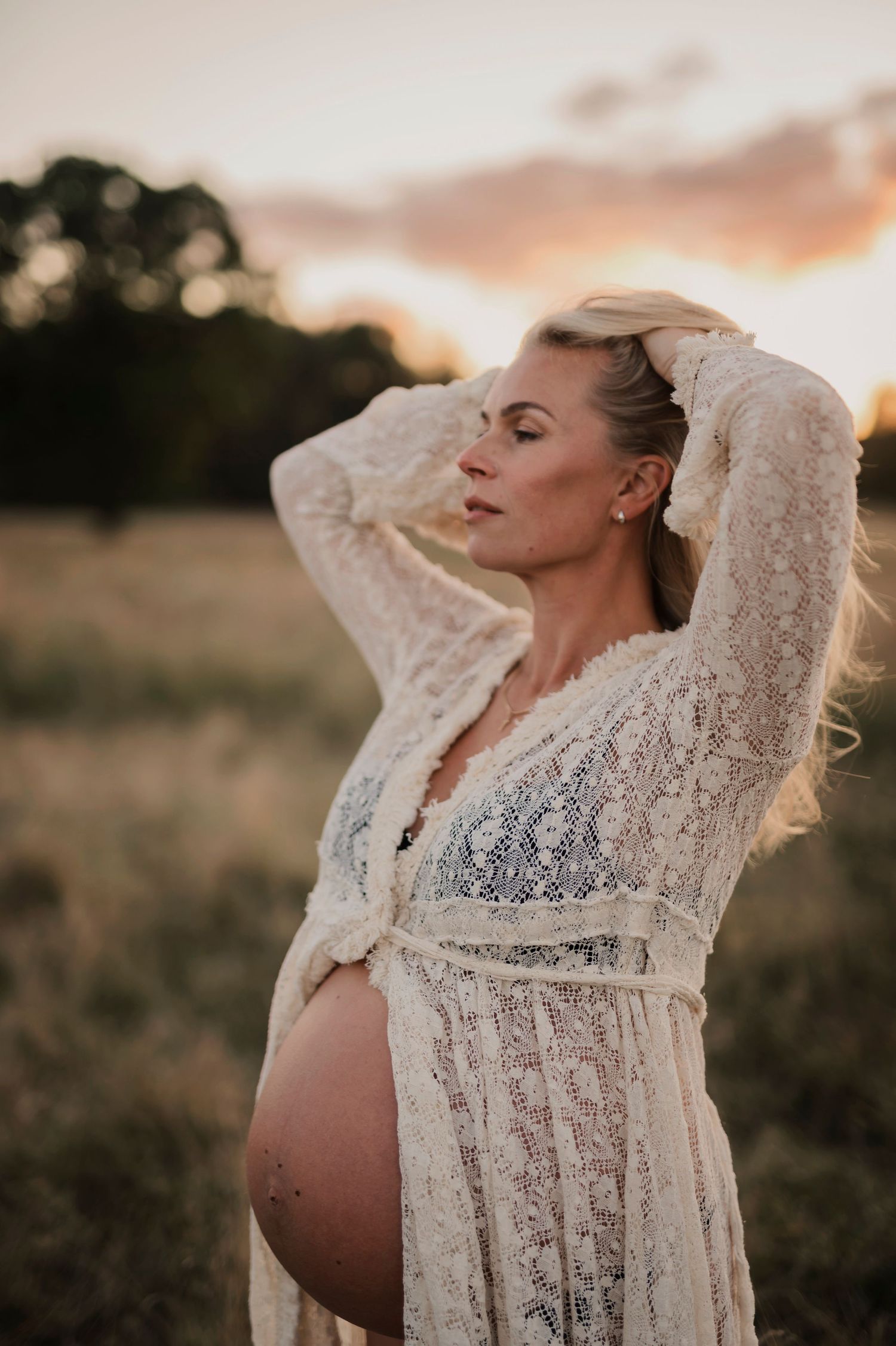 Gravidfotografering i Skåne med gravid kvinna i gyllene fält i solnedgång.
