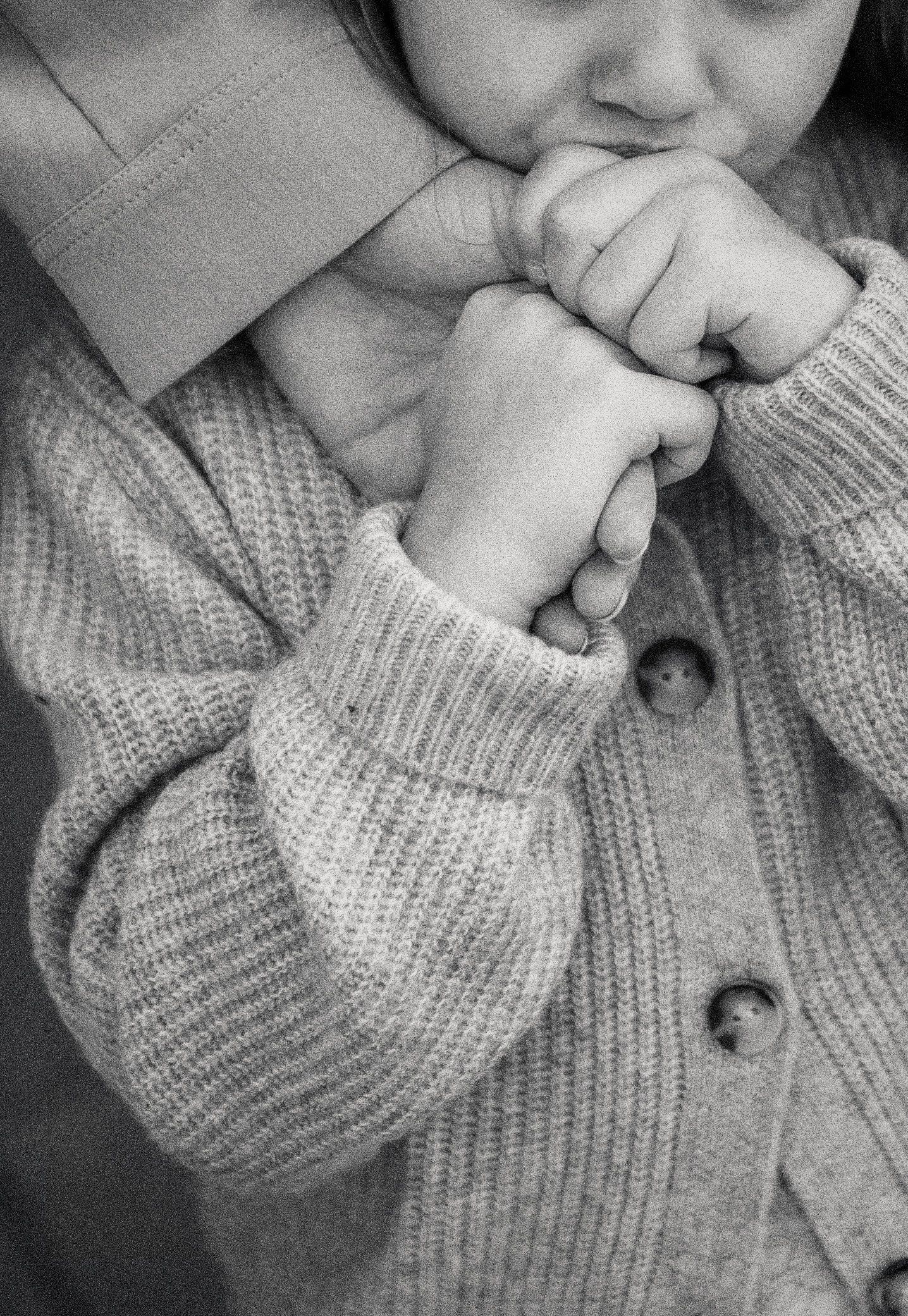 Familjefotografering i Skåne med barn som håller vuxens hand i svartvitt närbild i mjukt ljus.