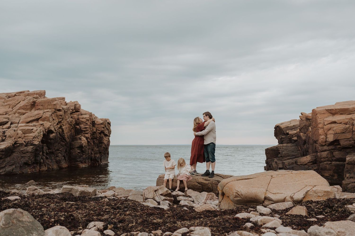 Family of four posing on rocky coastal shoreline with ocean and cloudy sky backdrop at hovs hallar