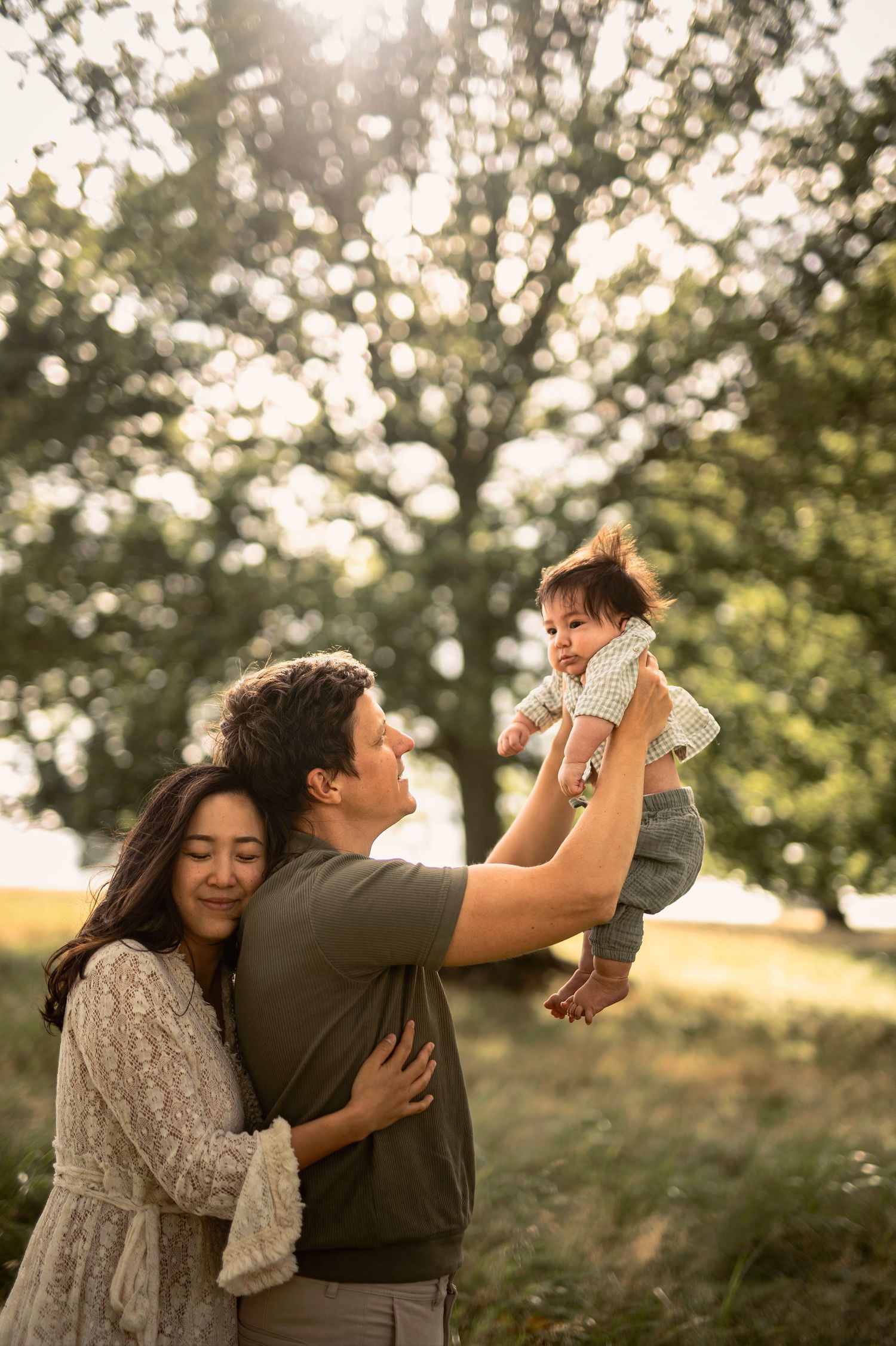 Familjefotografering i Skåne med föräldrar som lyfter sitt barn i solbelyst parkmiljö.