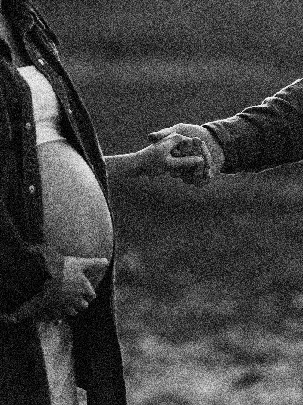 Svartvit detaljbild från en gravidfotografering i Skåne med två händer som möts i dramatiskt ljus.