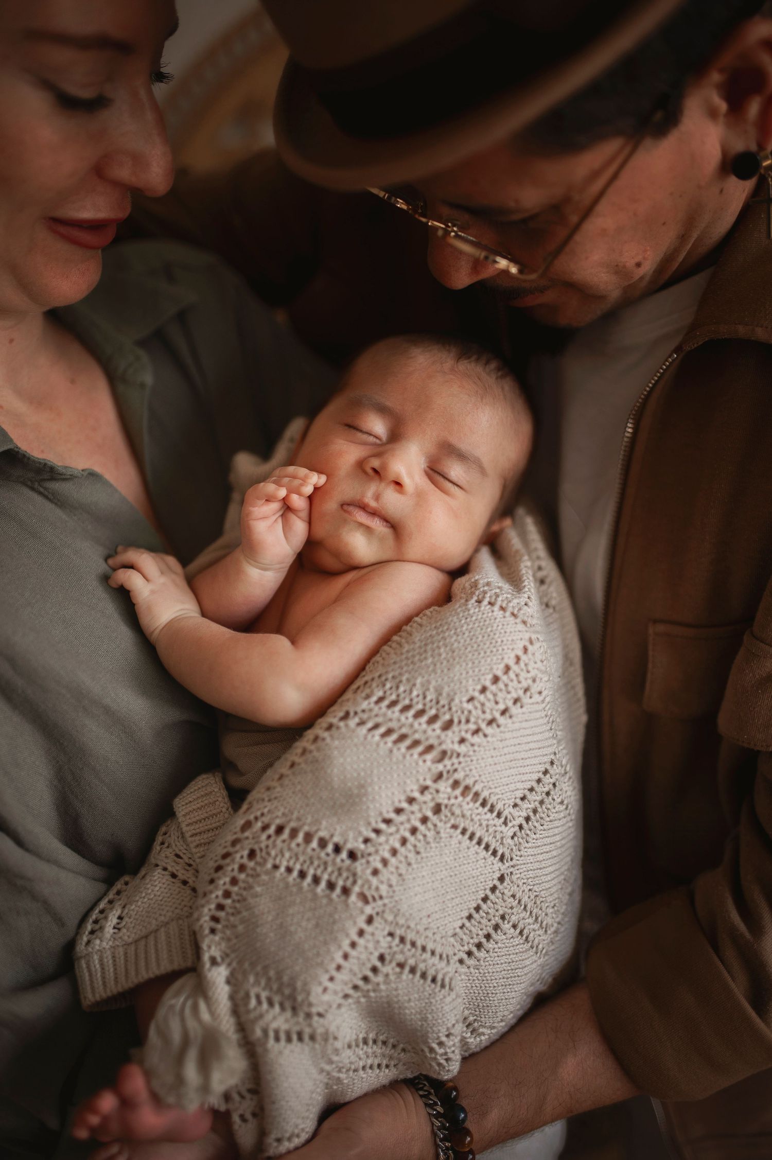Peaceful sleeping newborn wrapped in knit blanket held between two caregivers.