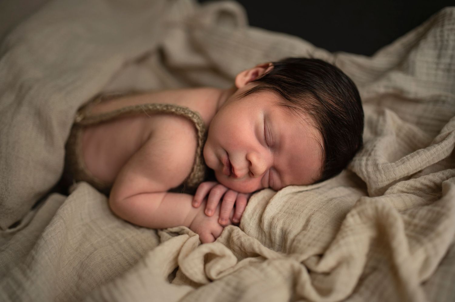 Sleeping newborn swaddled in soft beige fabric with gentle lighting in intimate portrait.