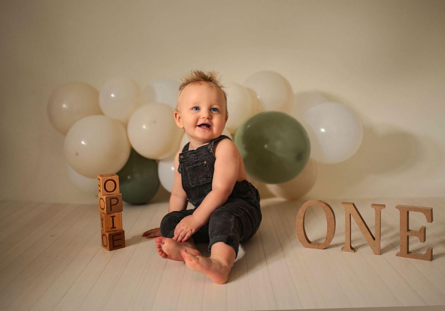 A joyful first birthday photo with balloons and wooden 'ONE' letters in the background.