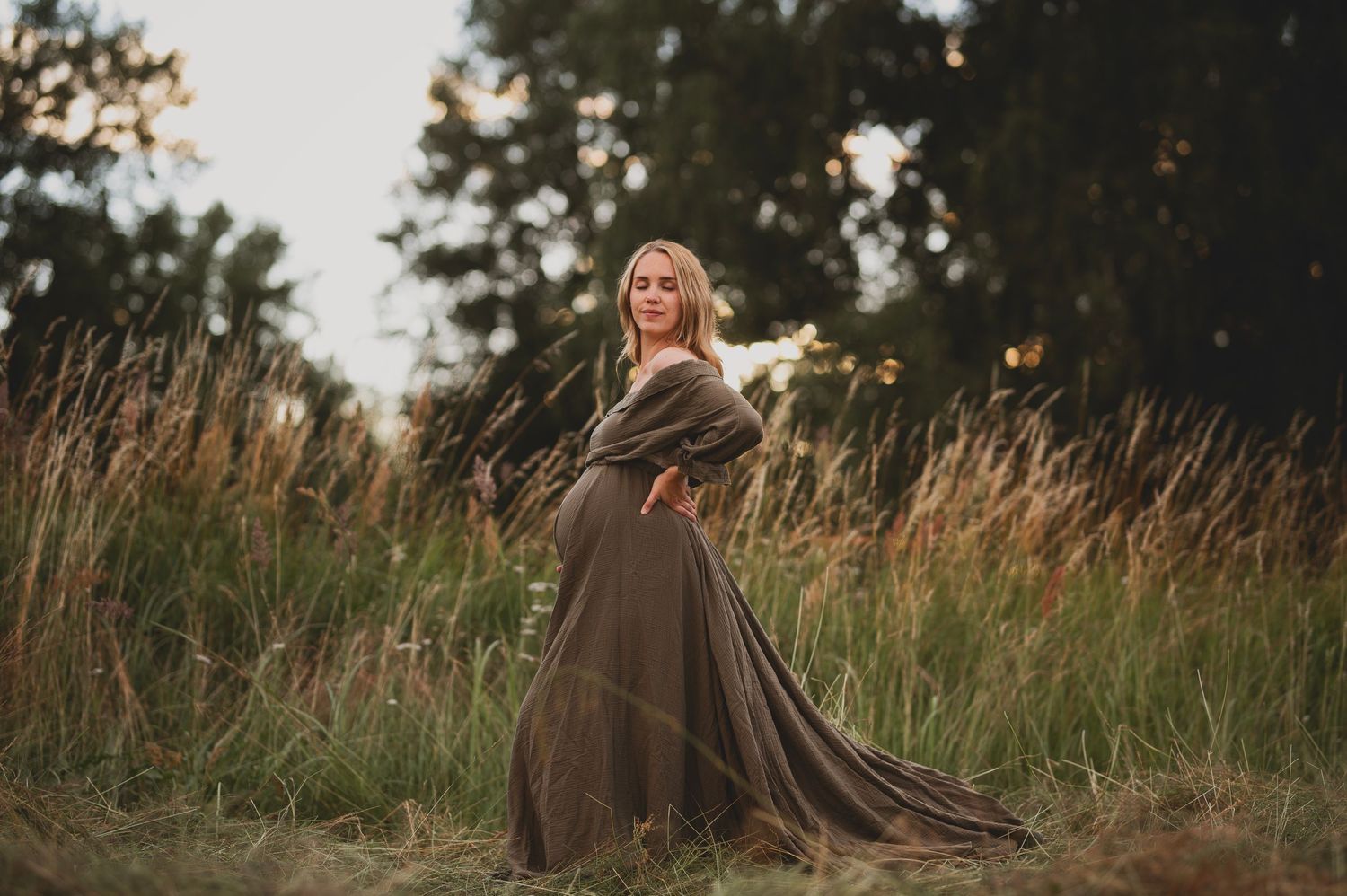 Gravidfotografering i Skåne med blivande mamma i grön flytande klänning som snurrar i gyllene fält vid solnedgång.