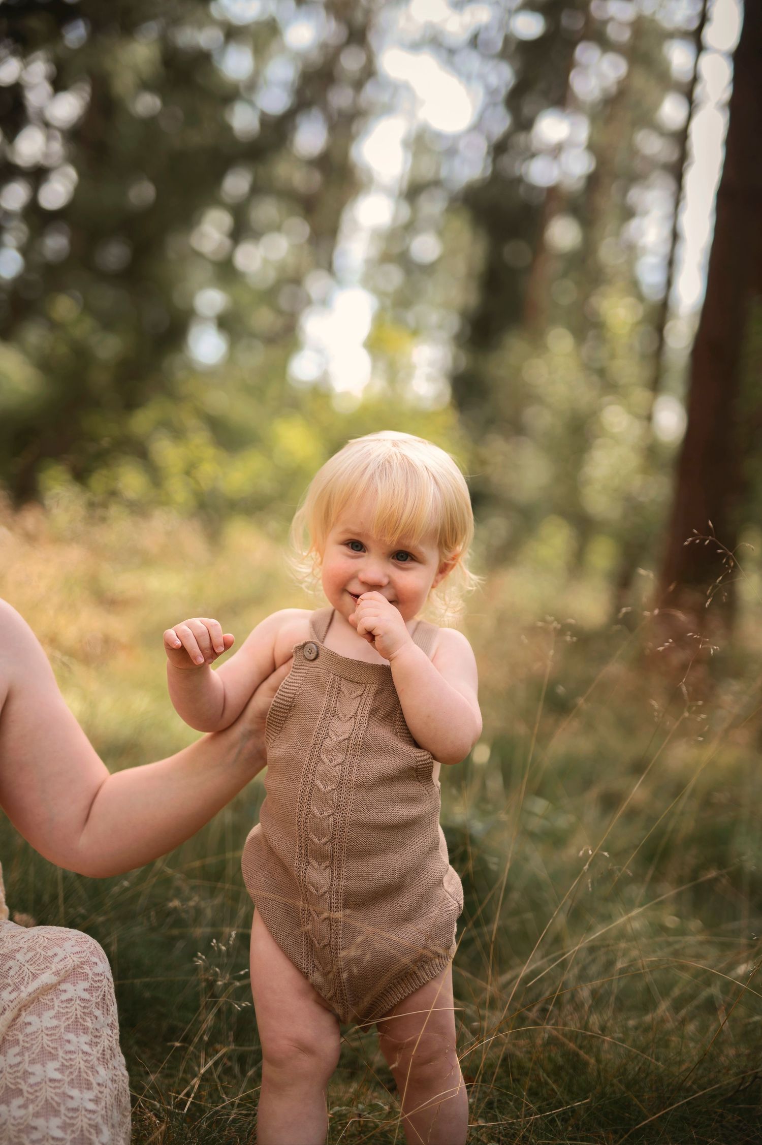 Moderskapsfotografering i Skåne med förälder som håller ett litet barn i spetsklänning i drömlik skogsmiljö.