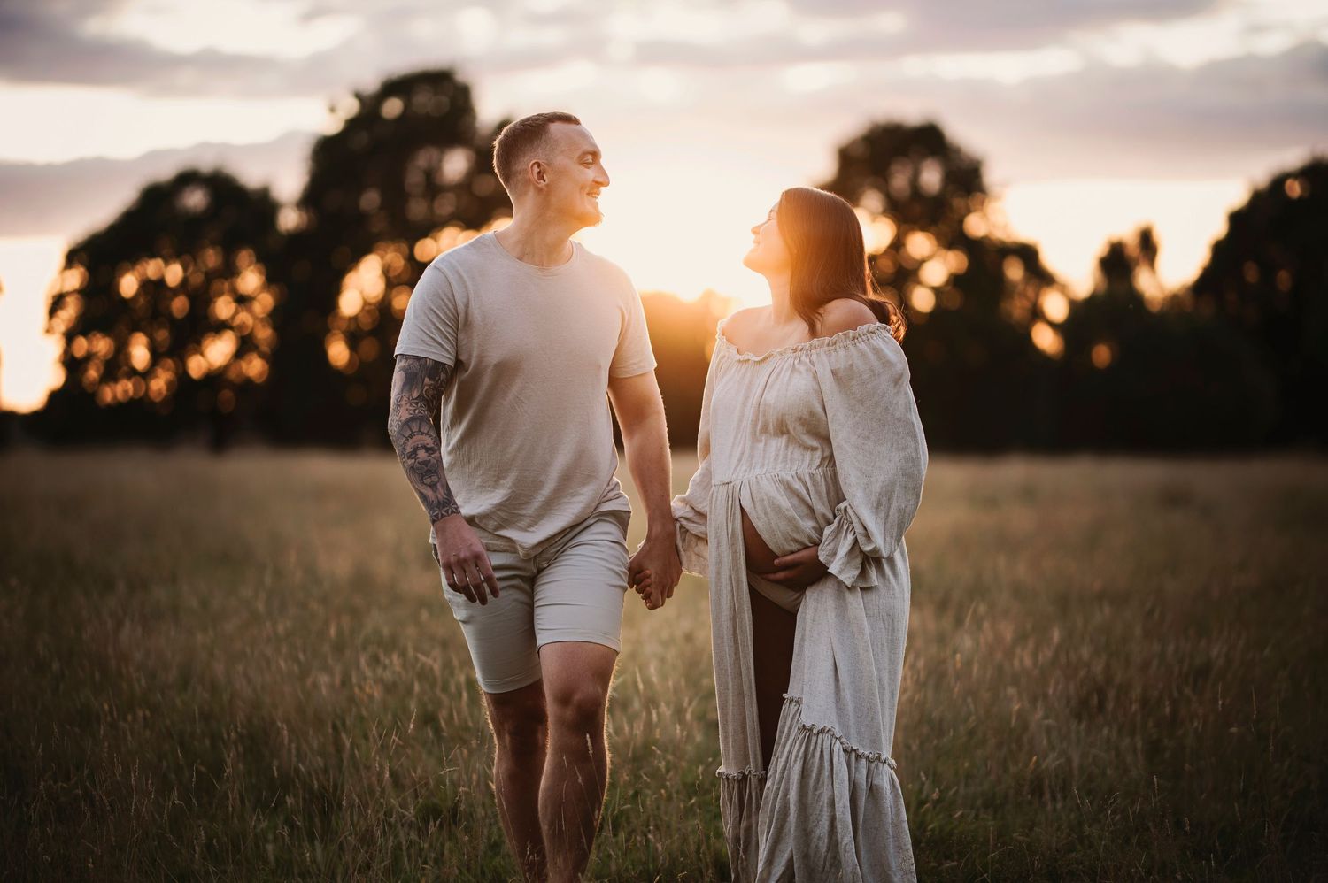 A couple shares a tender moment in a field during golden hour.