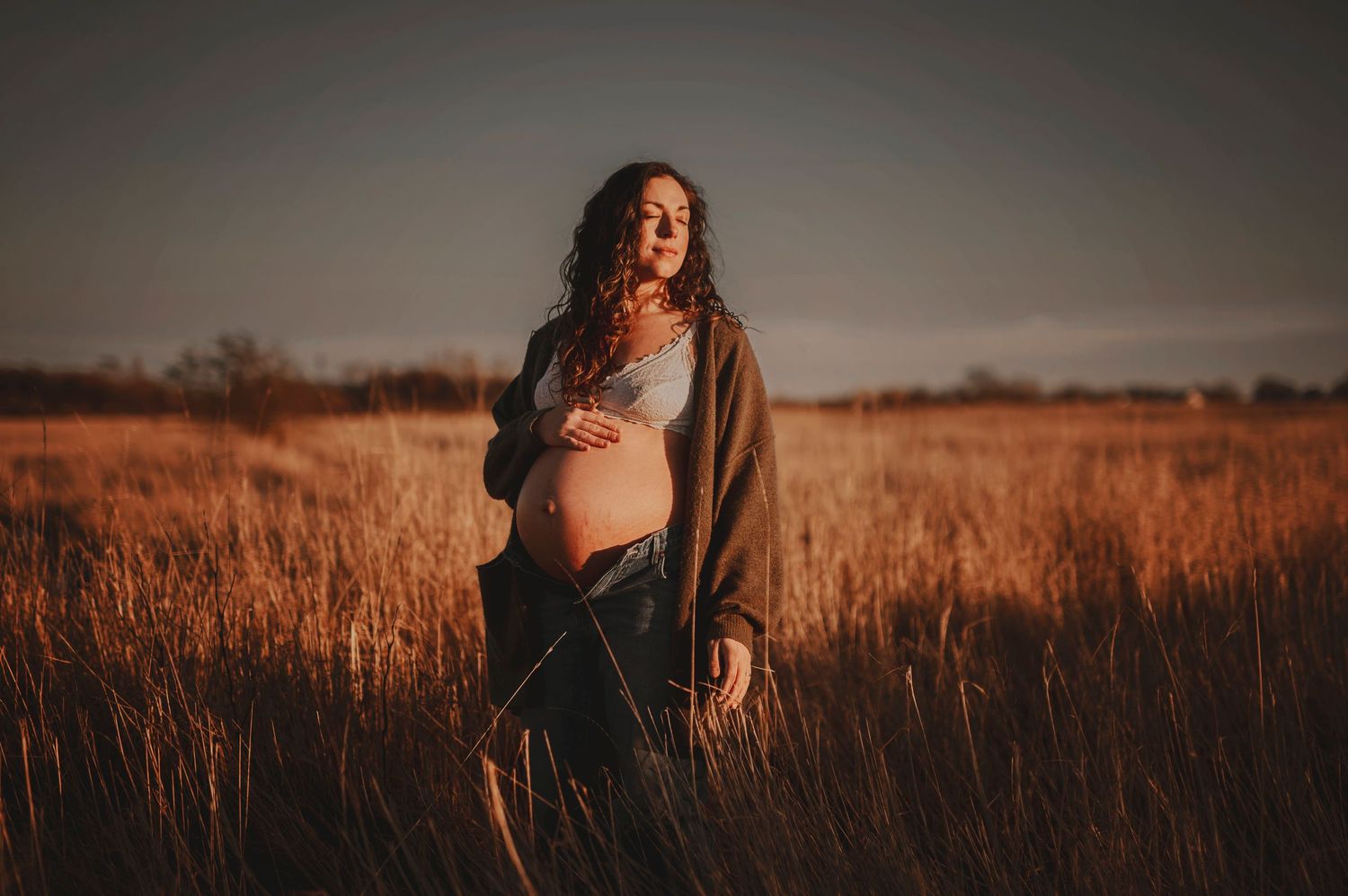 Gravidfotografering i Skåne med gravid kvinna i rustikt fält i kvällsljus i naturen.