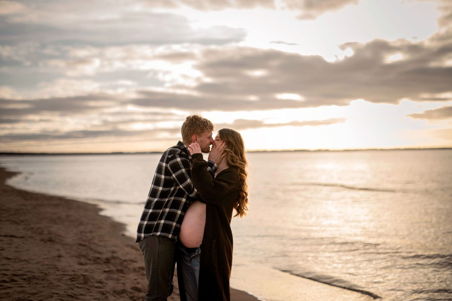 Gravidfotografering i Skåne med blivande föräldrar som kysser varandra vid havet i solnedgången.