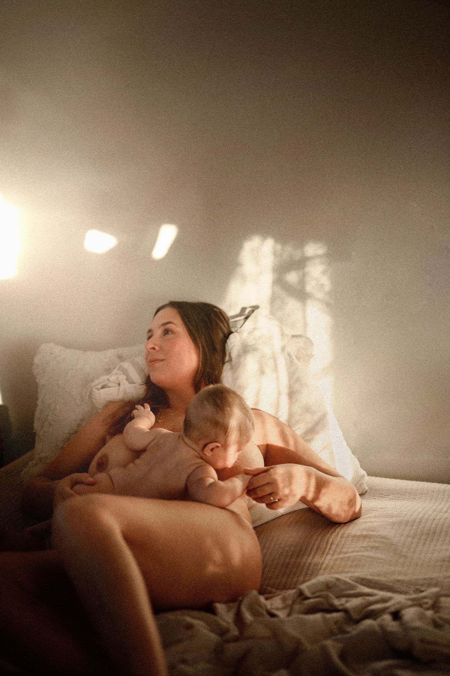 Amningsfotografering där en mamma ammar sin nyfödda bebis i ett varmt och naturligt ljusfylld studio.