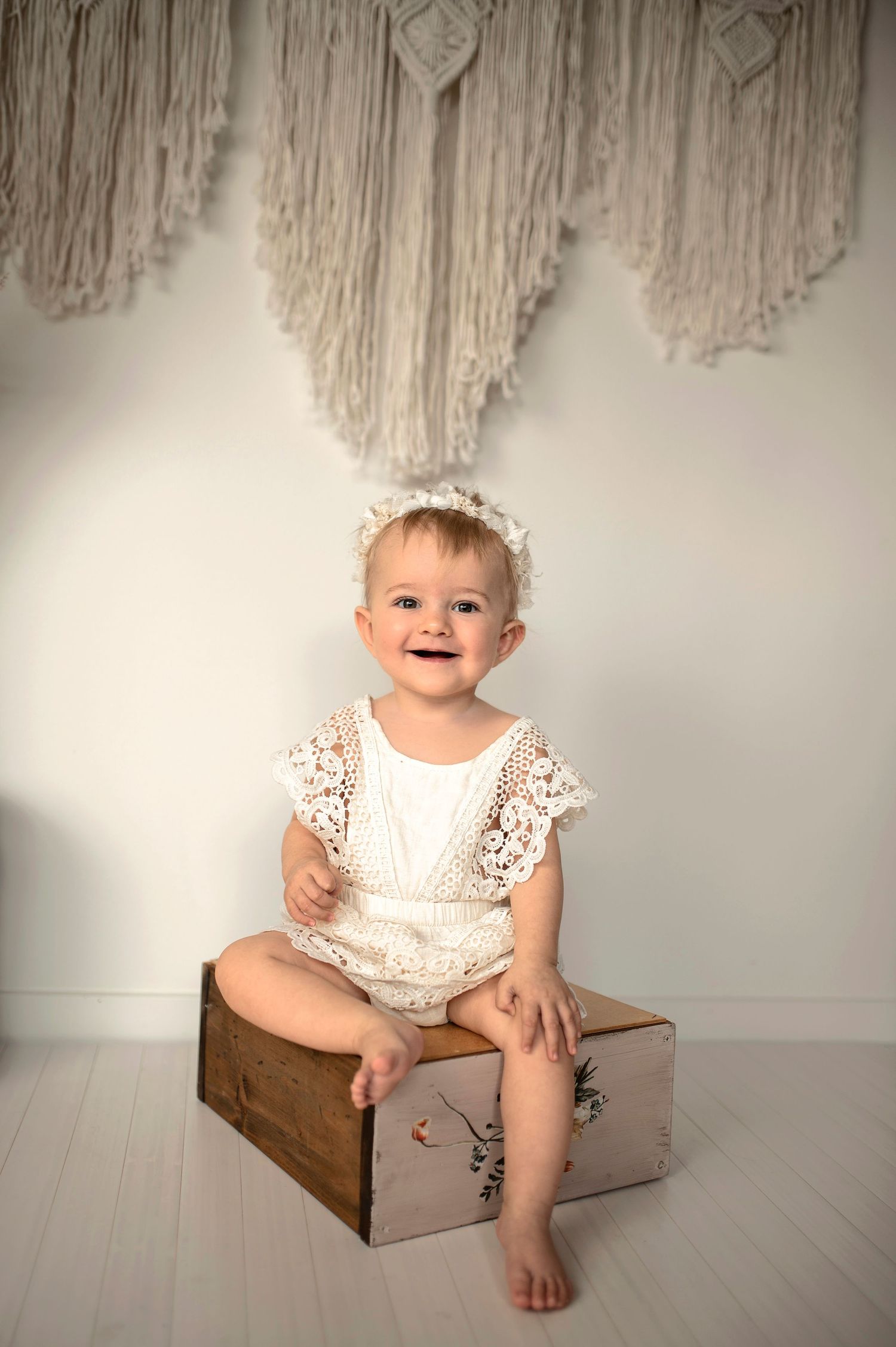 Leende bebis under en barnfotografering i studio i Hässleholm med bohemisk inredning och makramévägg.