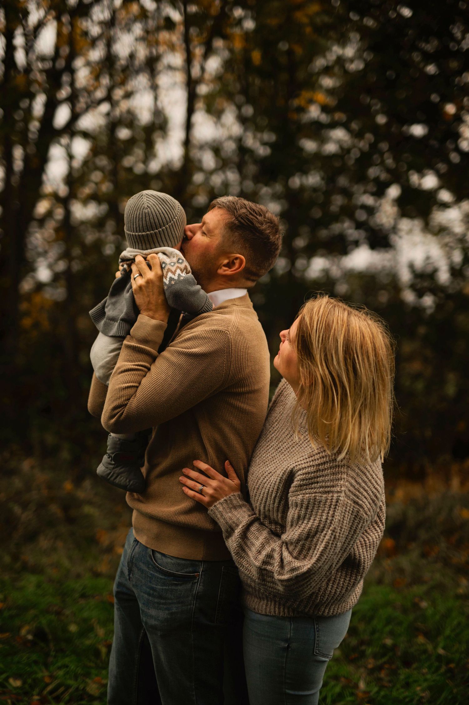 A couple shares a tender moment with their baby outdoors in autumn.