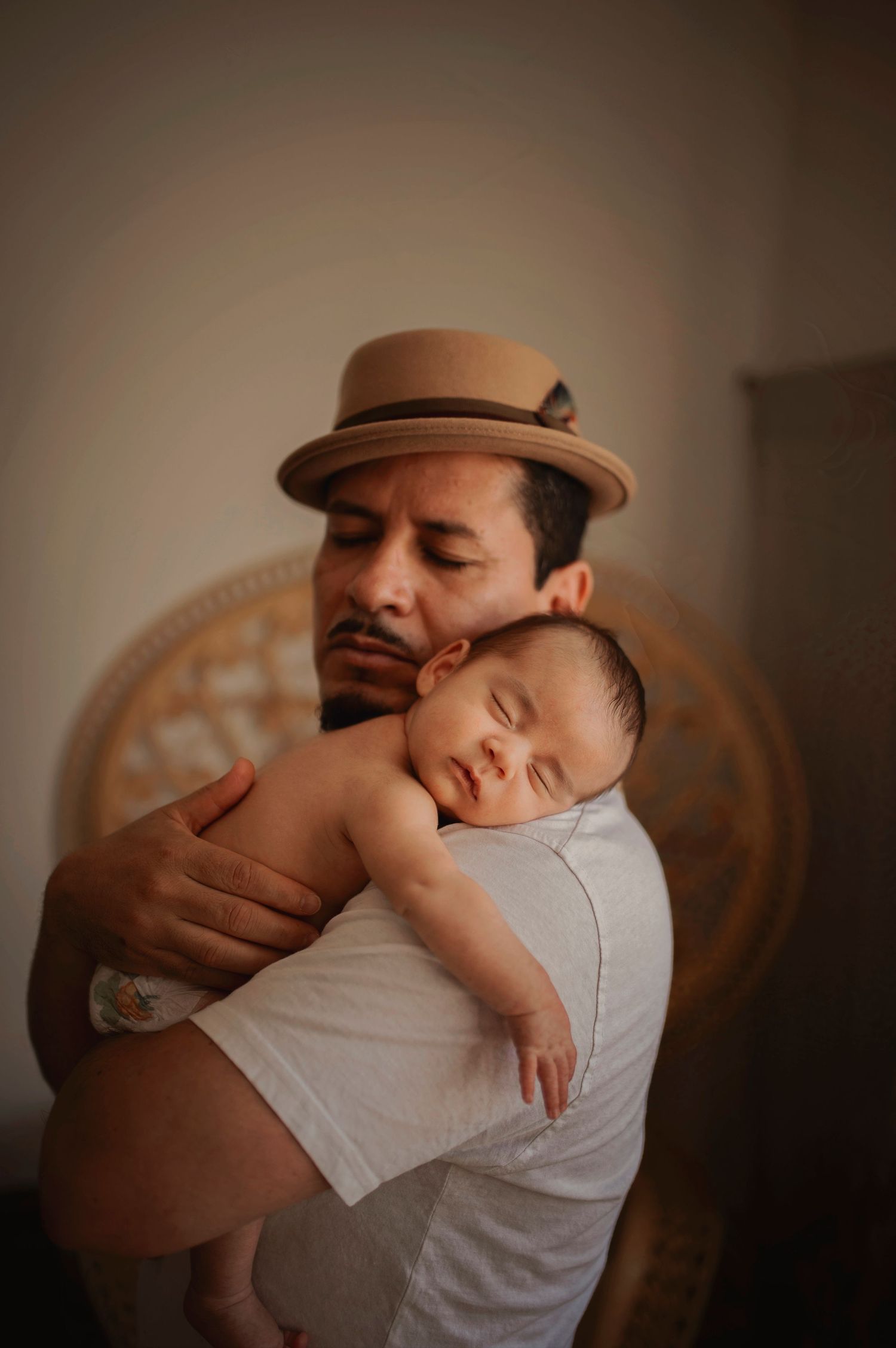 Parent wearing brown hat holding sleeping baby against decorative backdrop.