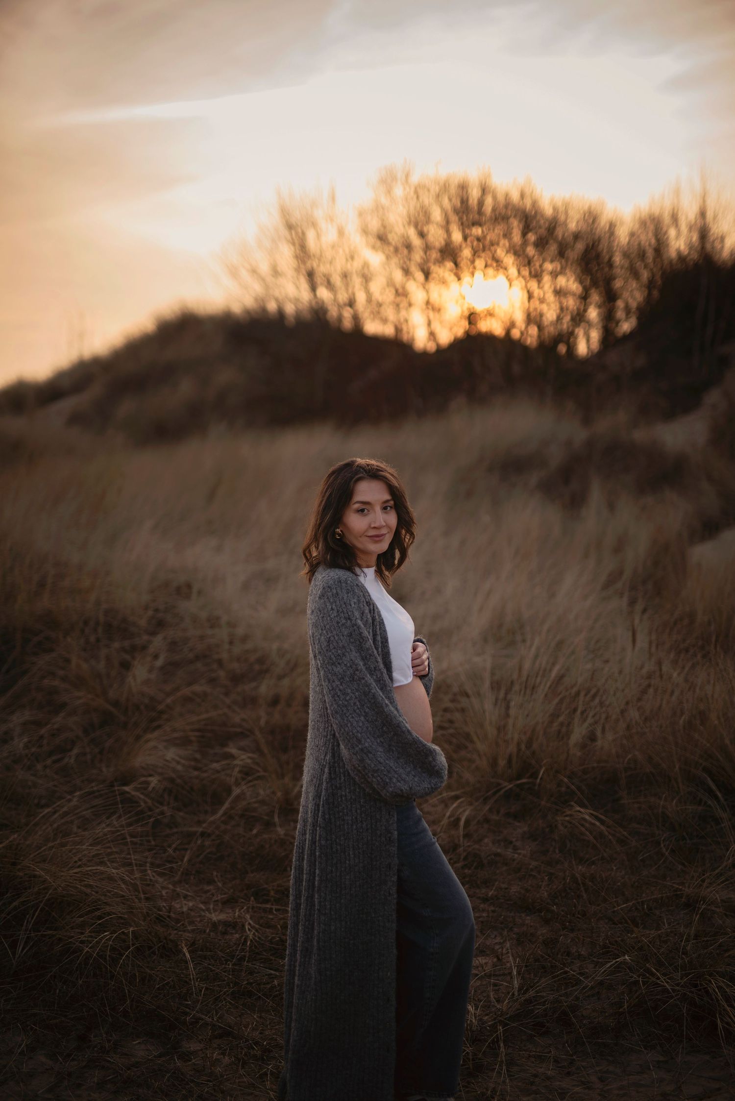 Silhouette of figure in long cardigan against golden sunset in tall grass.