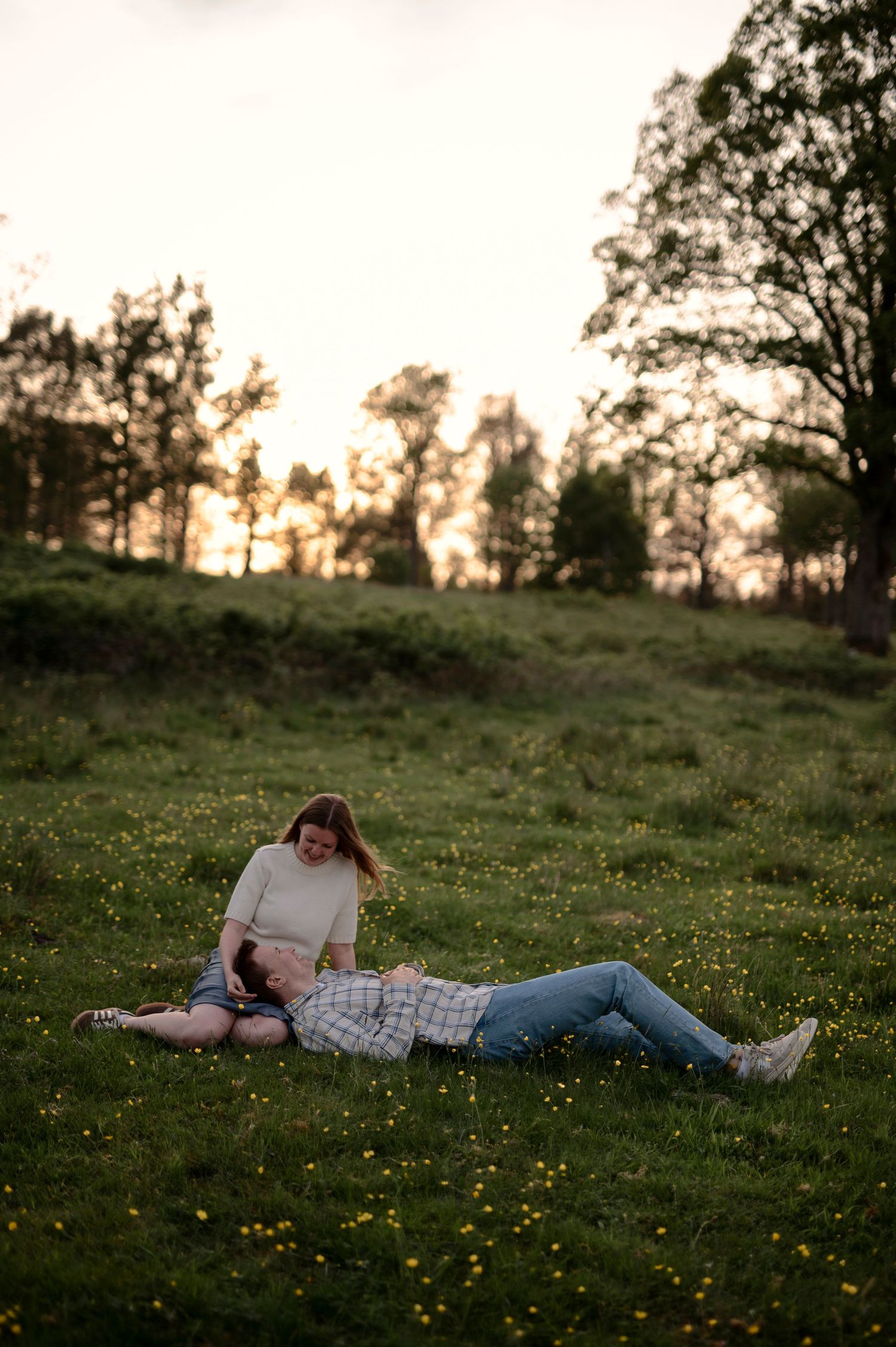 Parfotografering i Skåne där ett par sitter tillsammans i en blommande äng i solnedgången