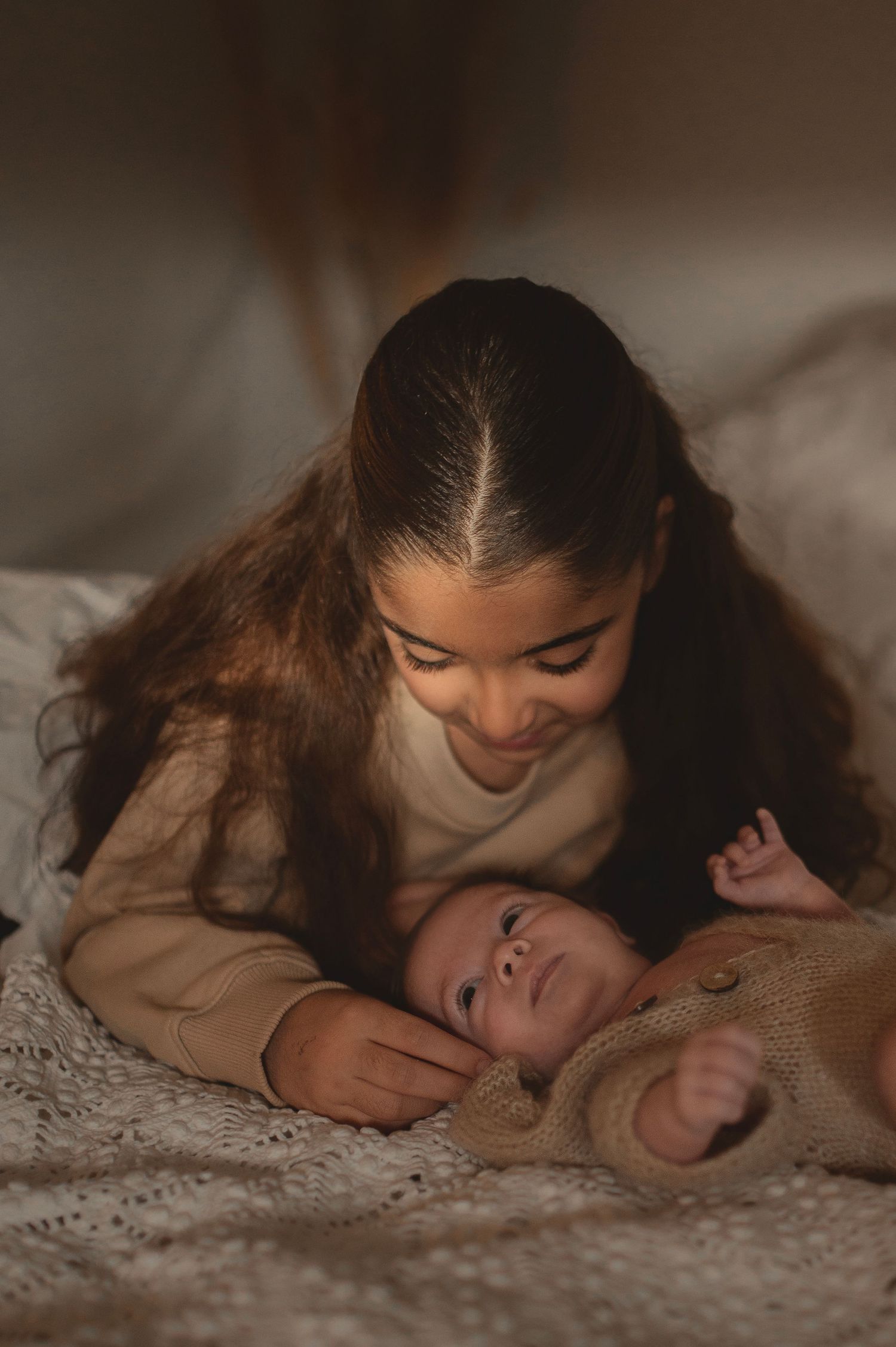 Tender moment between caregiver and infant on white textured bedding.