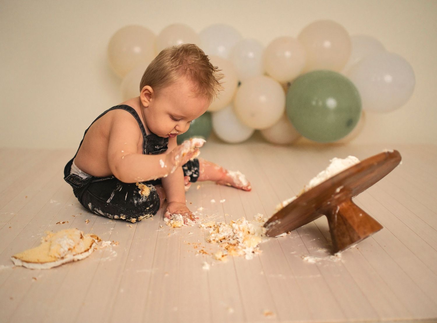 A cake smash photo showing scattered cake and frosting on a wooden platform.
