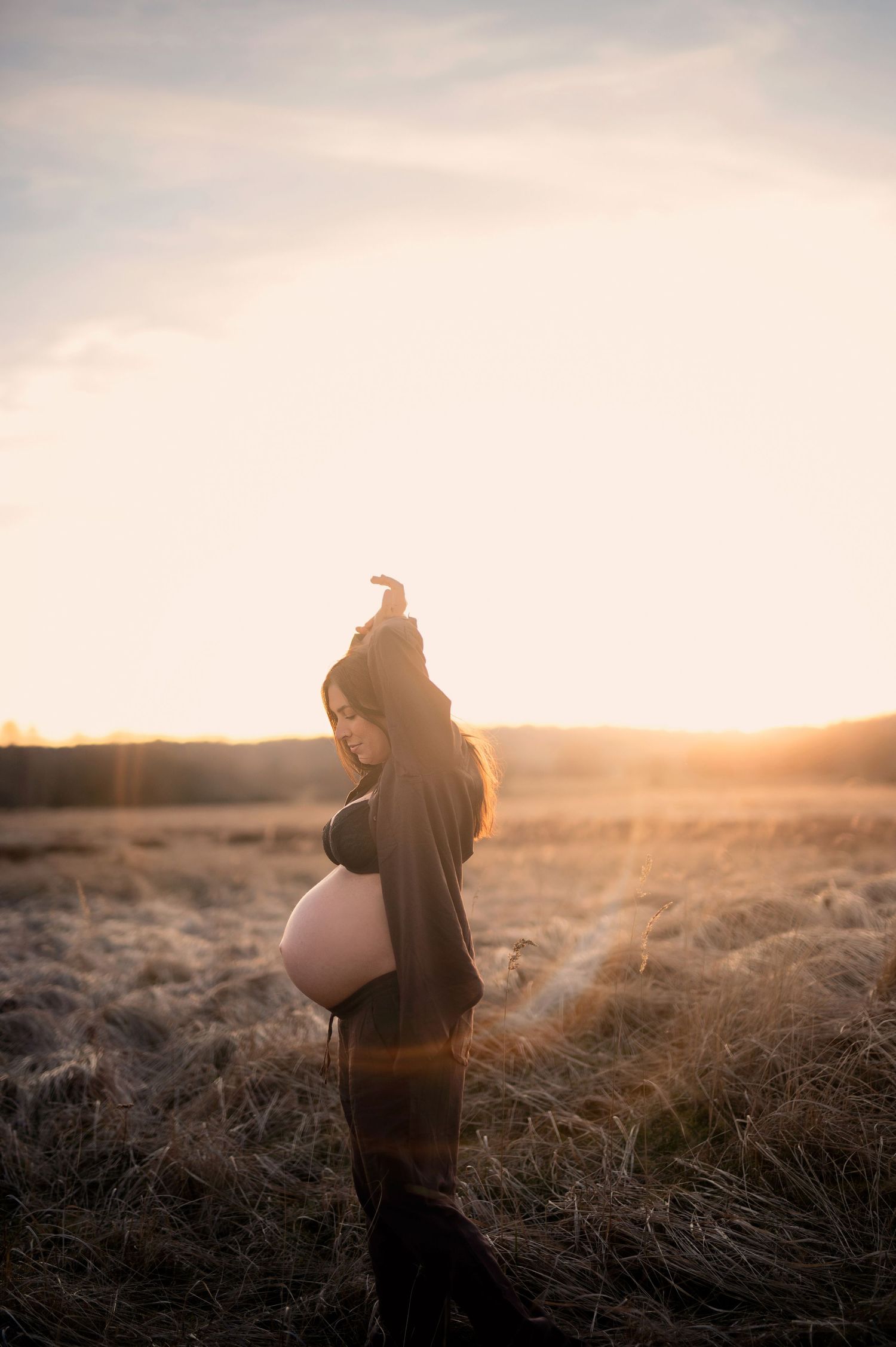 Gravidfotografering i Skåne med gravid kvinna i gyllene fält i solnedgång.