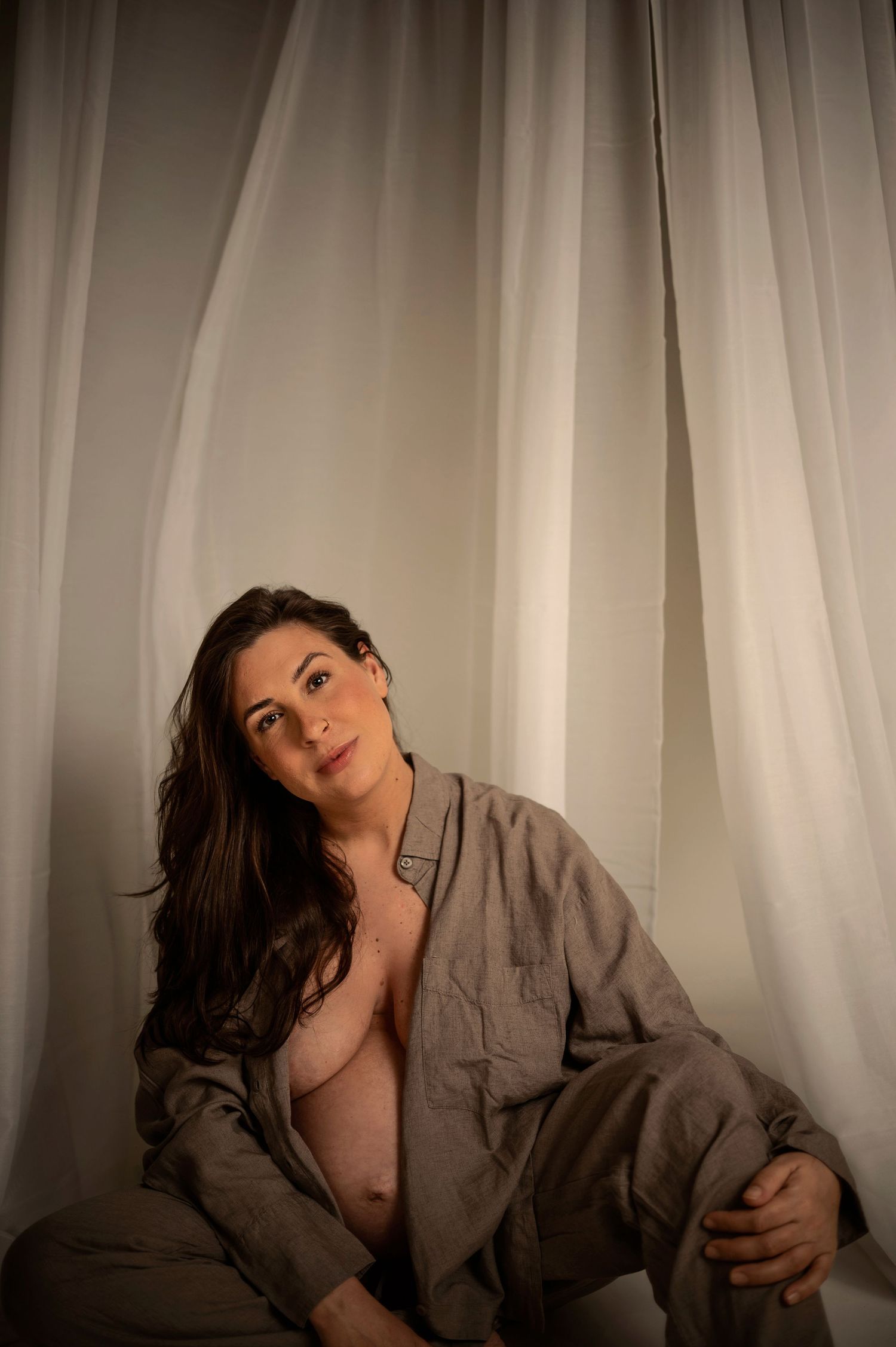 Gravidfotografering i Hässleholm med en gravid kvinna i mjukt studioljus framför ljusa gardiner.