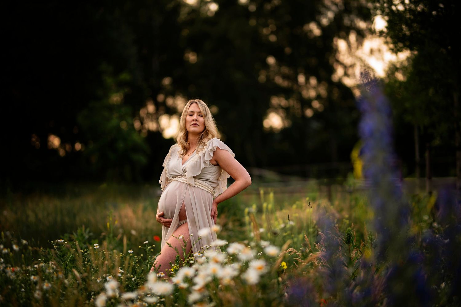 Gravidfotografering i Skåne med blivande mamma i blomsteräng i gyllene solnedgång.
