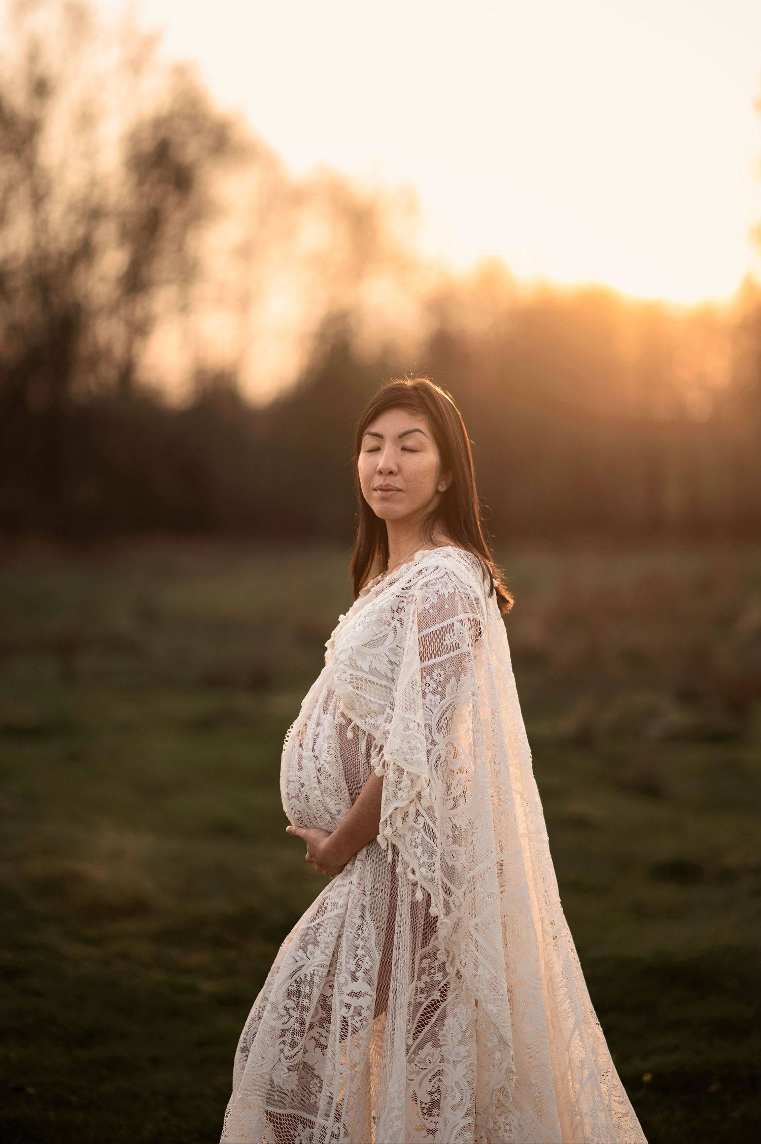 Gravid kvinna i spetsklänning under en gravidfotografering i Skåne vid solnedgången