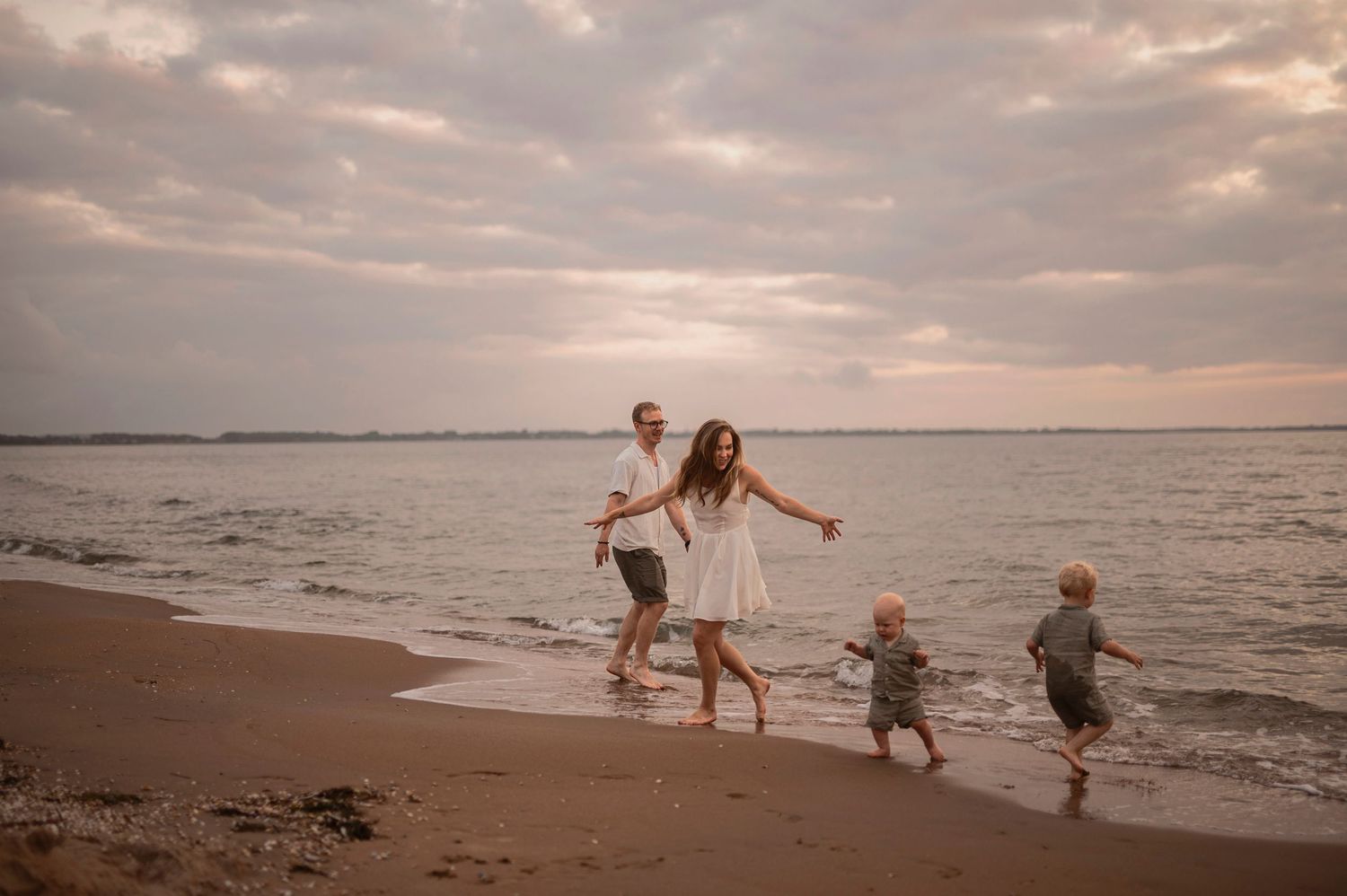 Happy family running and playing together on a sandy beach at sunset.