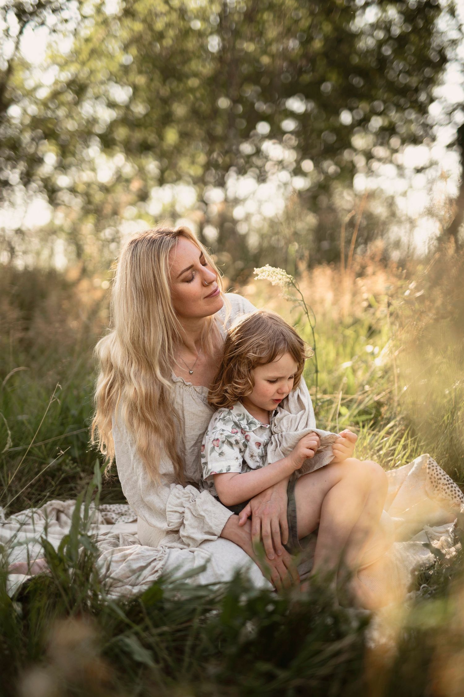 Familjefotografering i Skåne med mamma som håller sitt barn i solbelyst äng i gyllene kvällsljus.